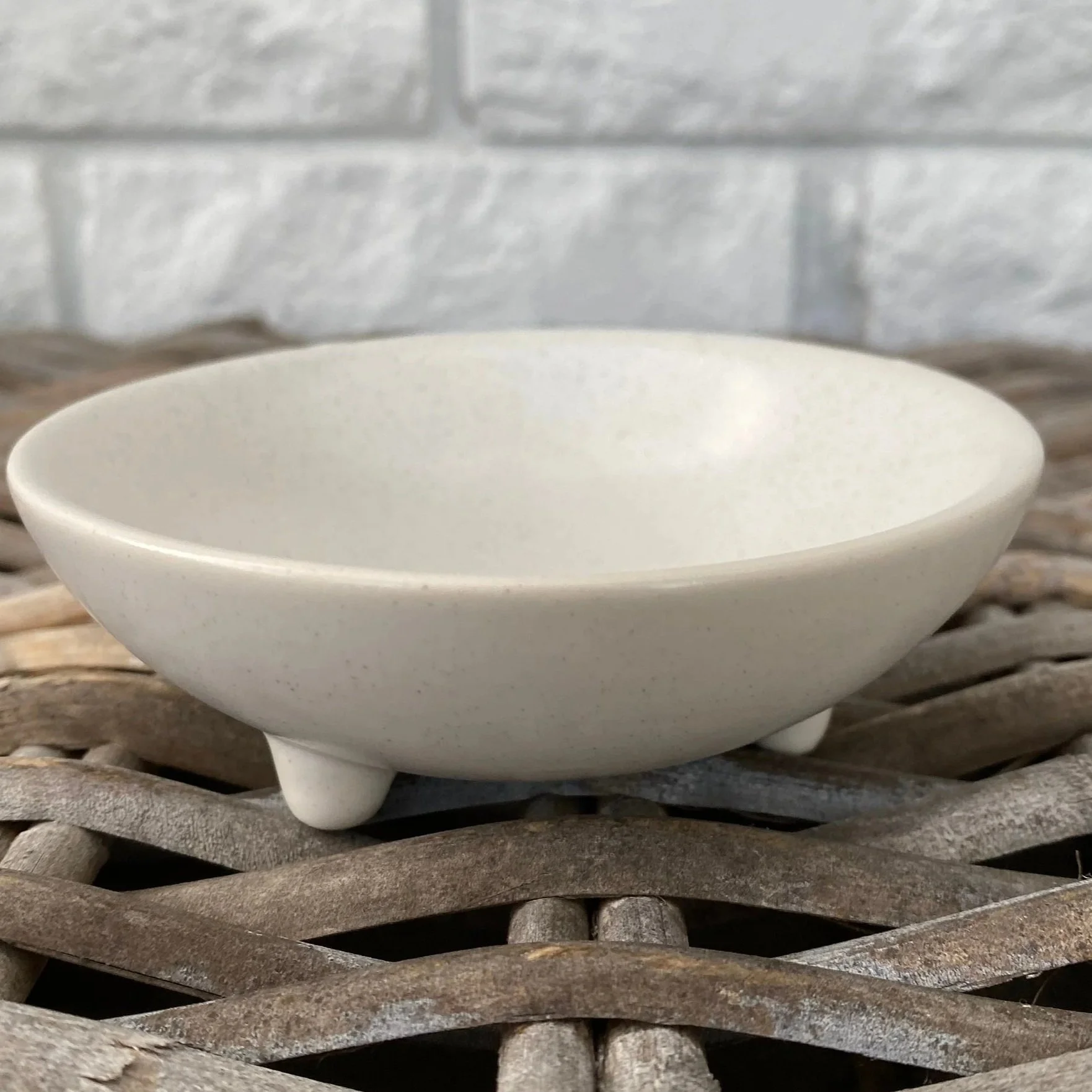 Side view of the white ceramic soap dish showing the shallow bowl shape and raised feet