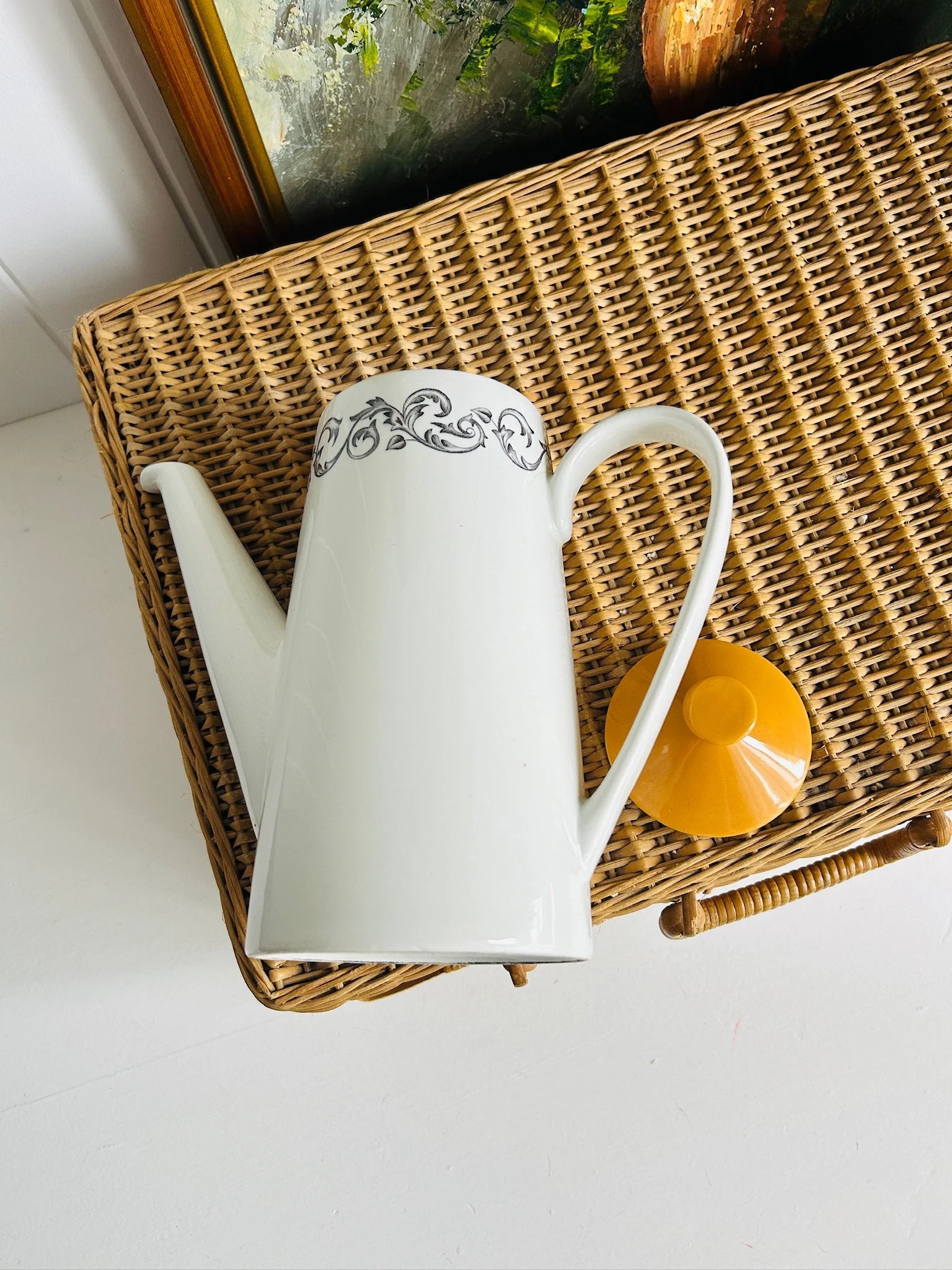 Overhead view of the Johnson Brothers DJ 100 coffee pot beside its matching orange lid, showing the long spout, curved handle, and black scrollwork rim pattern.