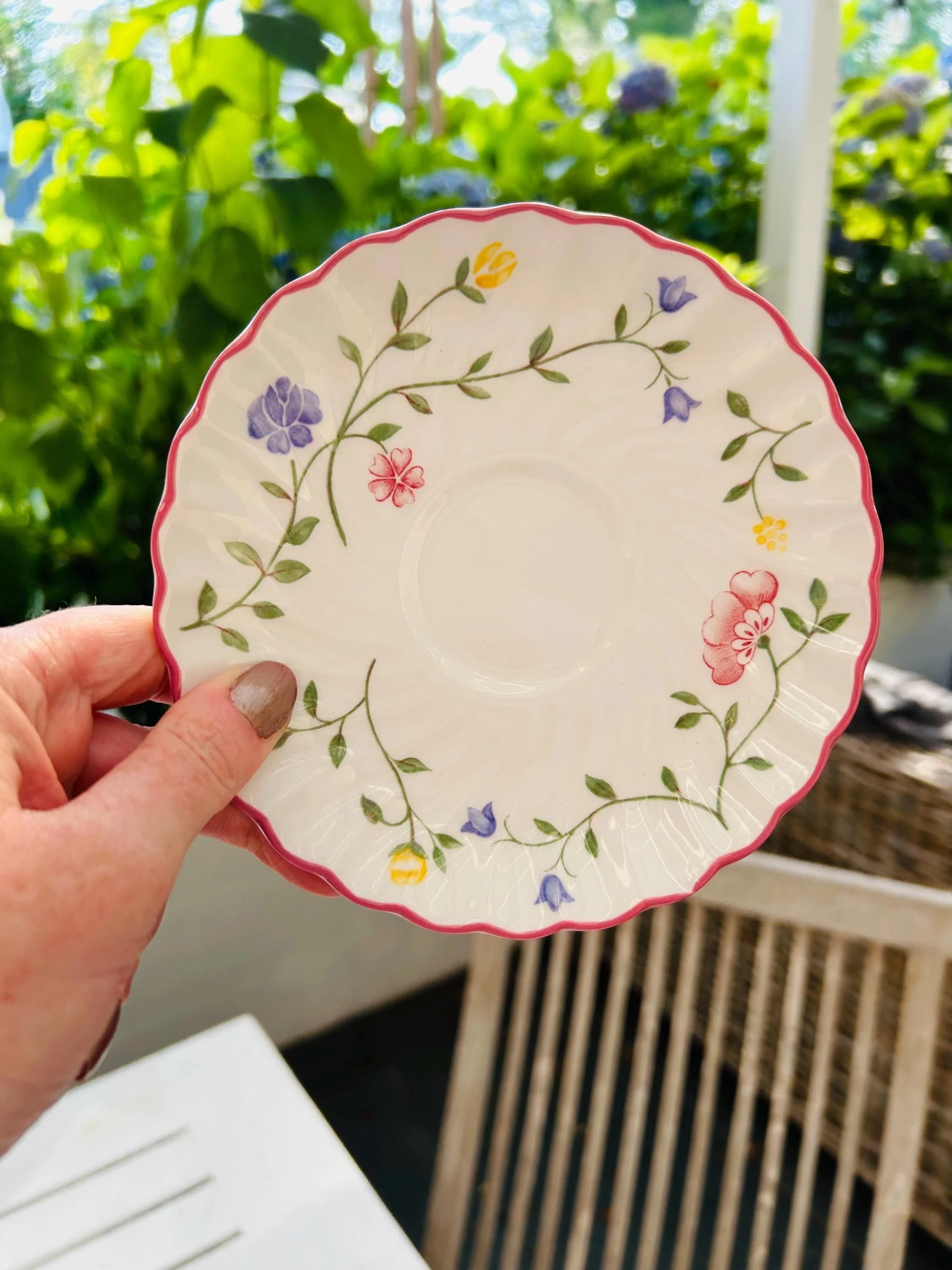 Single saucer held in hand, showing floral motif and scalloped pink rim