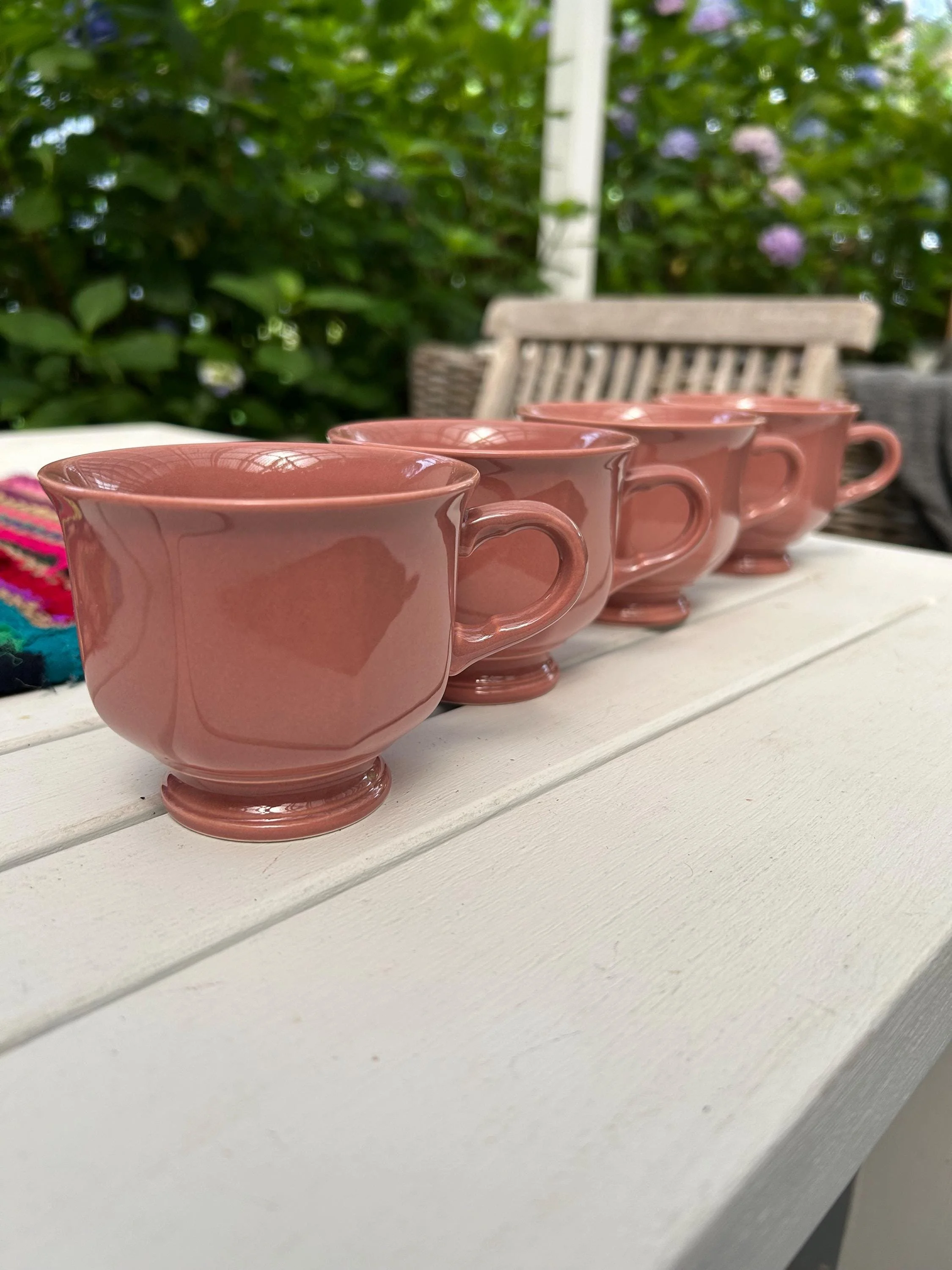 Full set of cups arranged in a row on table with green foliage backdrop