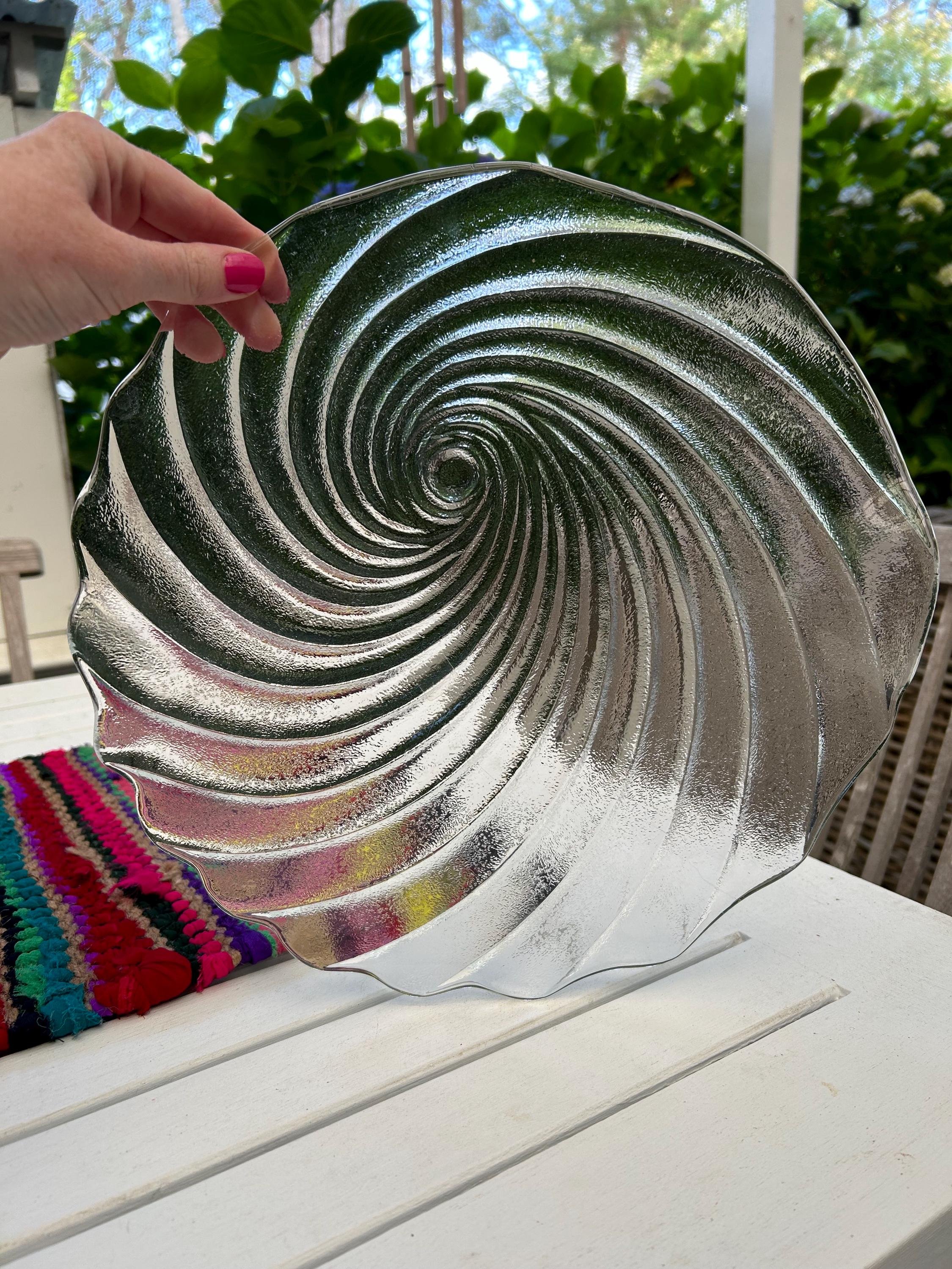 Hand holding platter outdoors displaying swirling shell design.