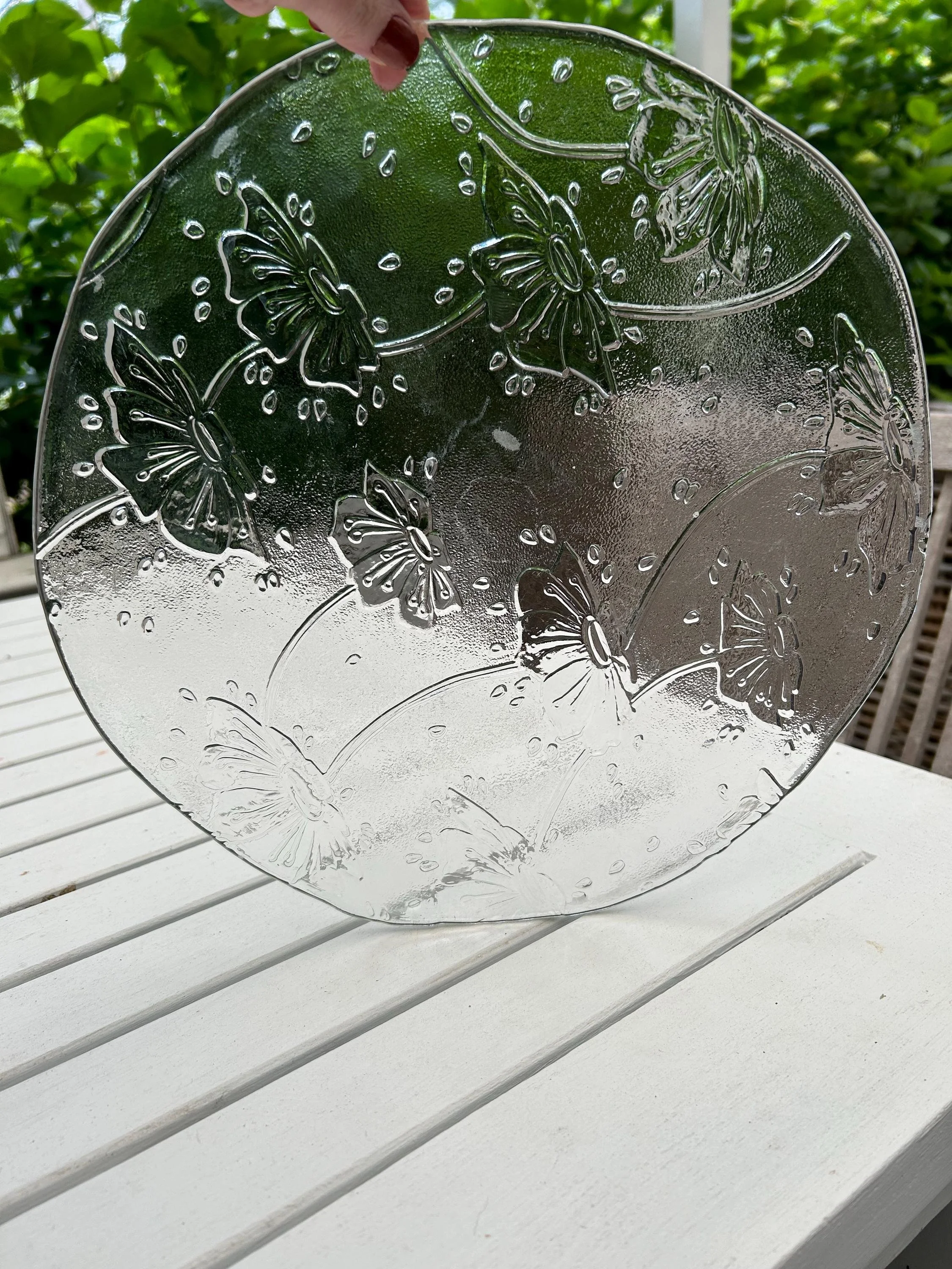 Cive Milano vintage clear glass platter with embossed butterfly and floral design held up to the light outdoors