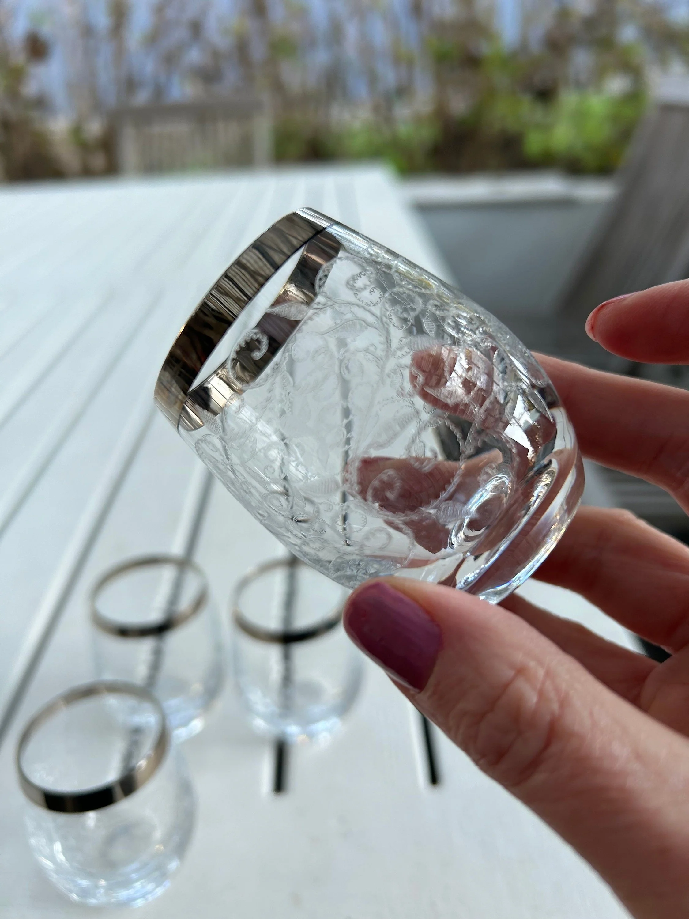 Close-up of one etched shot glass with silver rim held in hand, outdoor lighting