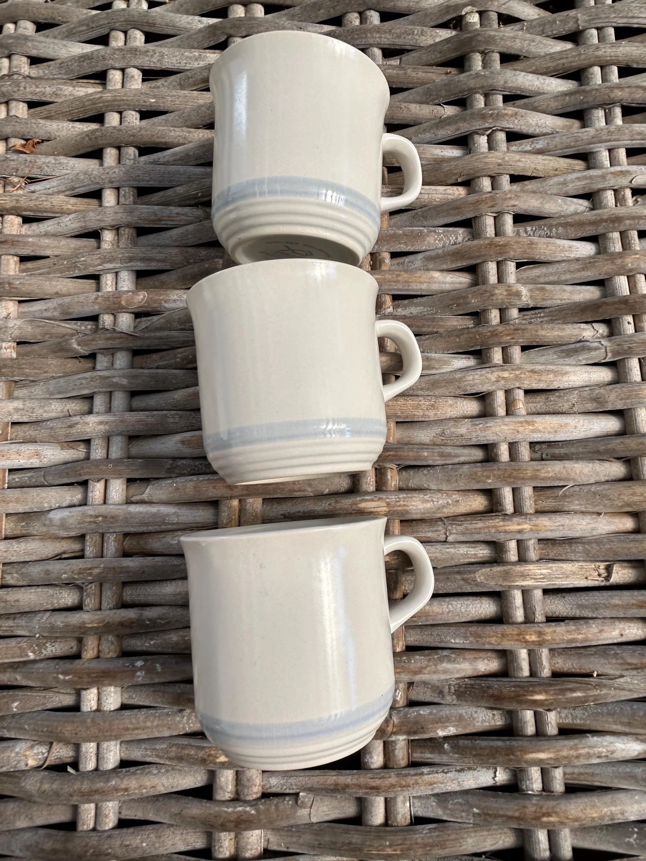 Stack of three mugs with soft blue-grey rims and curved handles