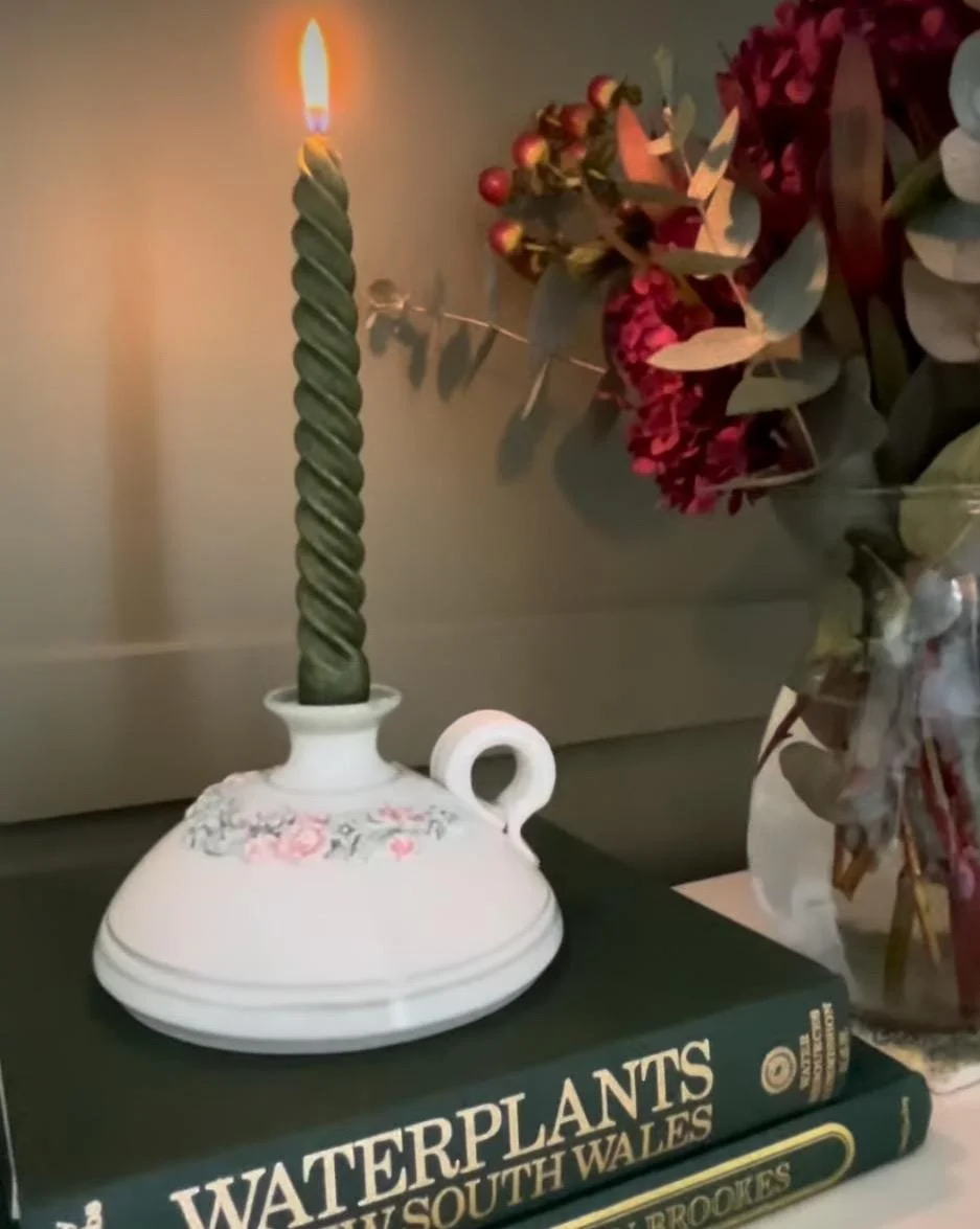 Styled image with lit taper candle in holder and floral background