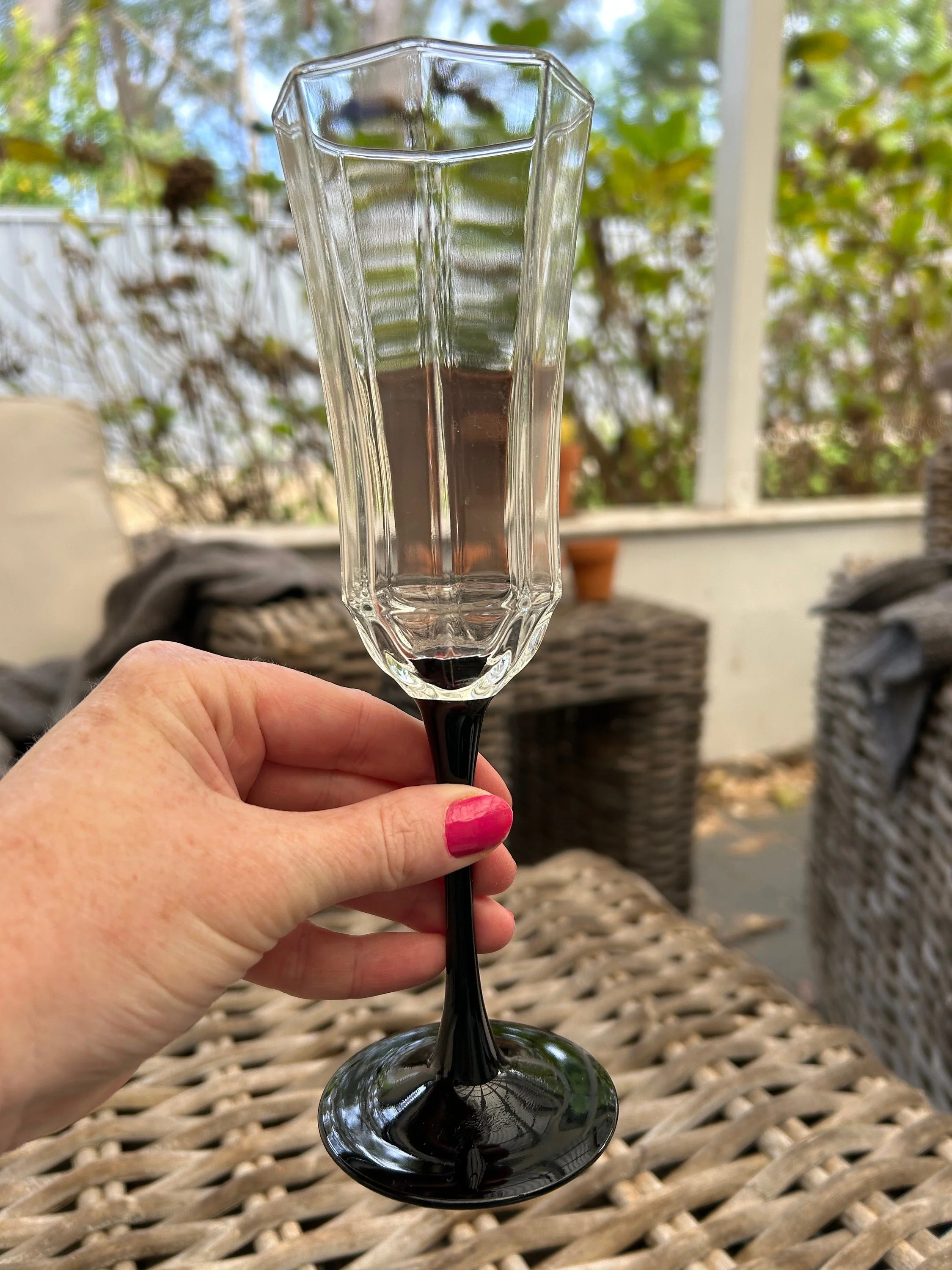 Single champagne glass held to show clear faceted bowl and black stem