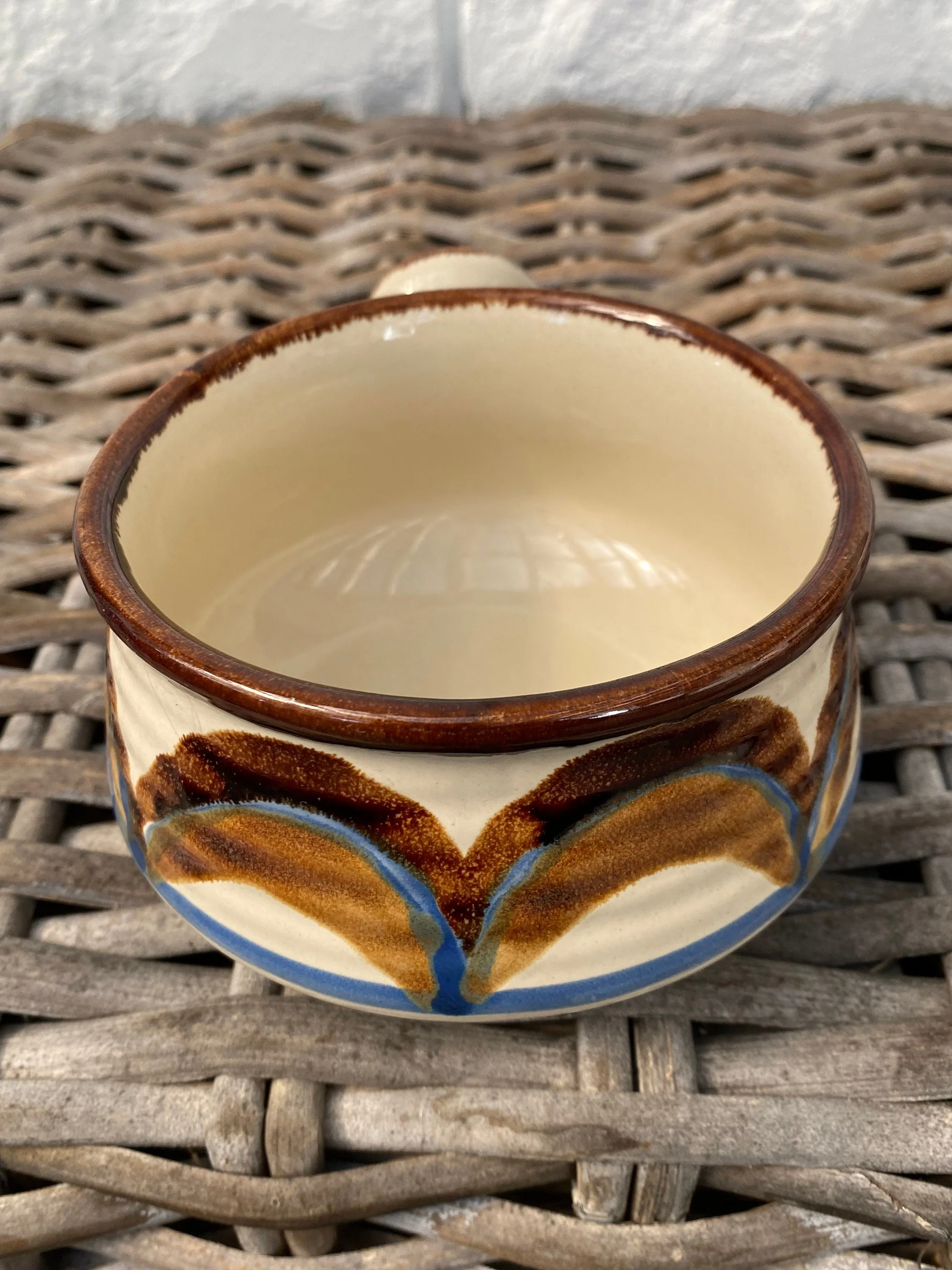 Front view of vintage handled stoneware soup bowl with brown rim and brown-blue decorative motif