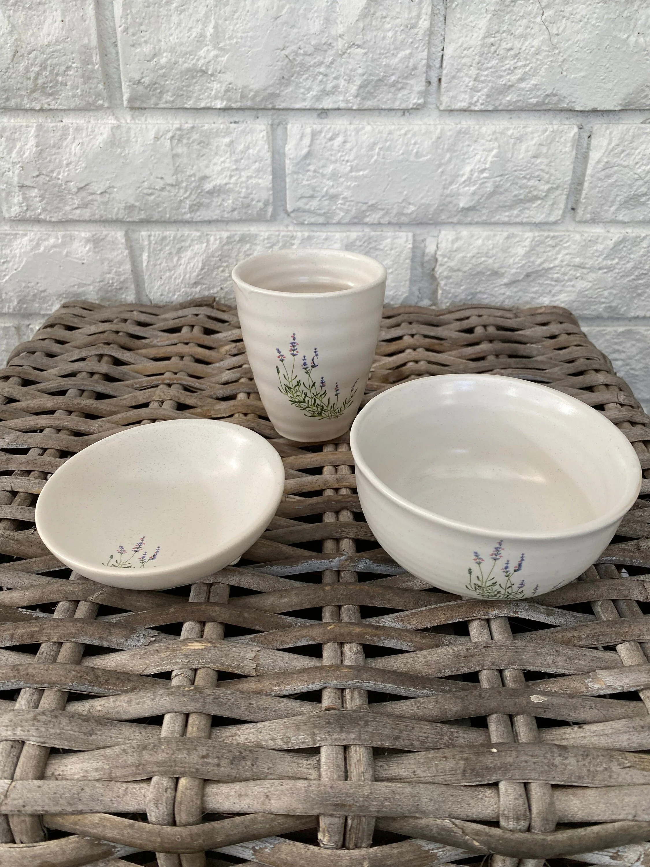 White ceramic lavender set with bowl, cup, and soap dish arranged together on a woven surface