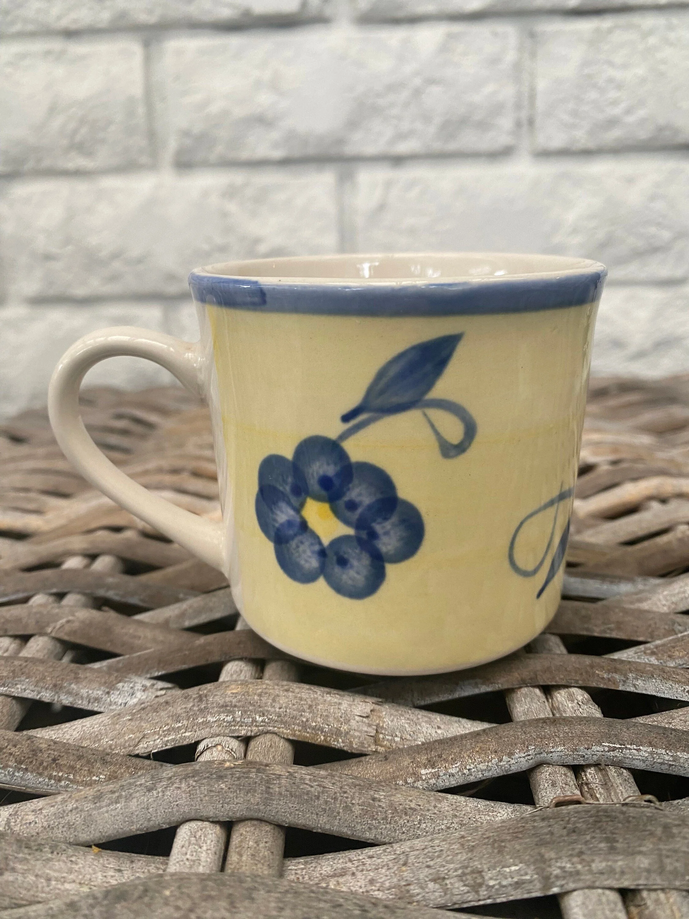 Side view of stoneware mug showing blue floral pattern, curved handle, and soft yellow glaze