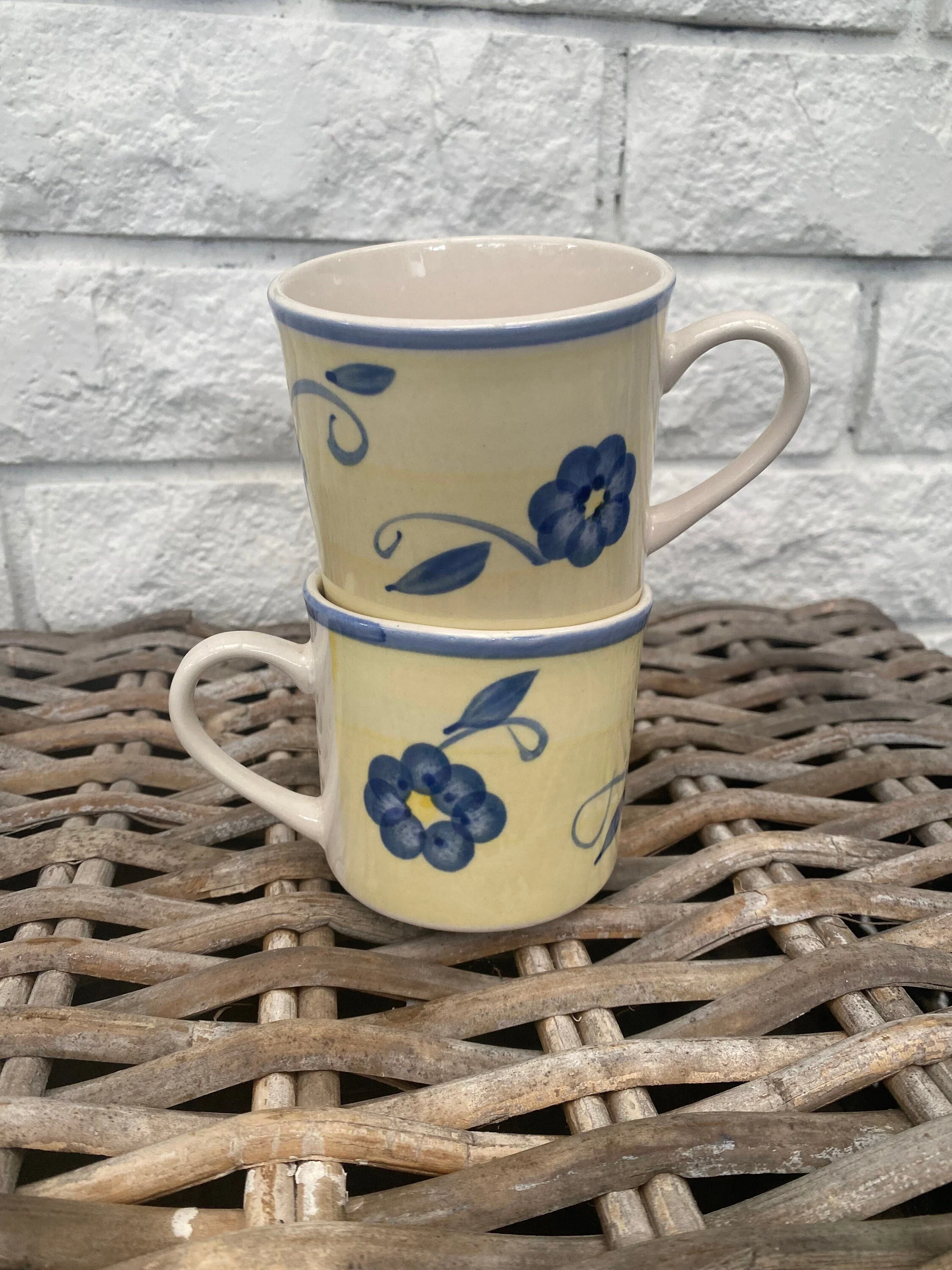 Two yellow and blue floral stoneware mugs stacked together for display