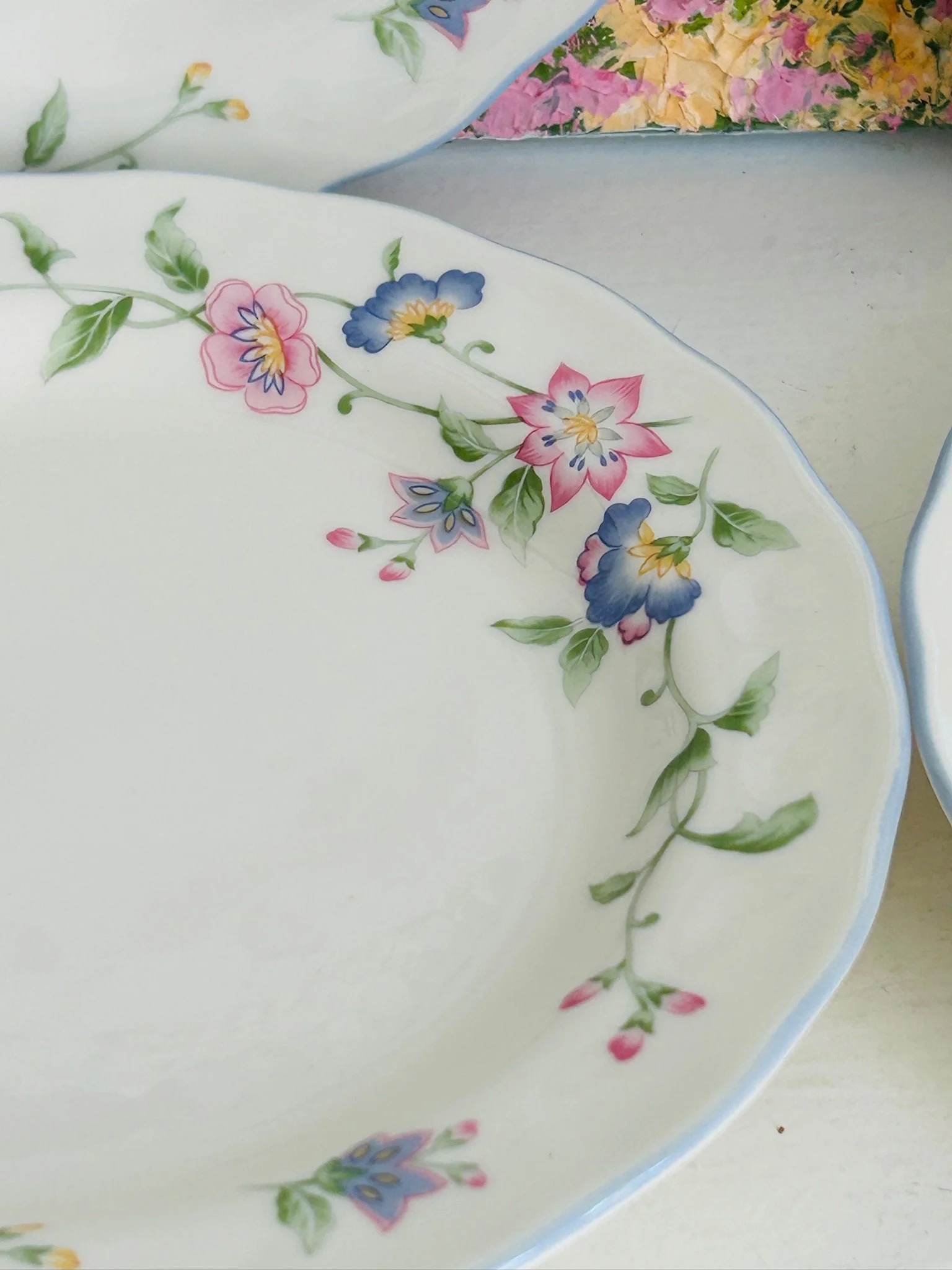 Close-up of the floral spray on the plate border featuring pink and blue blossoms with green leaves on white fine china.