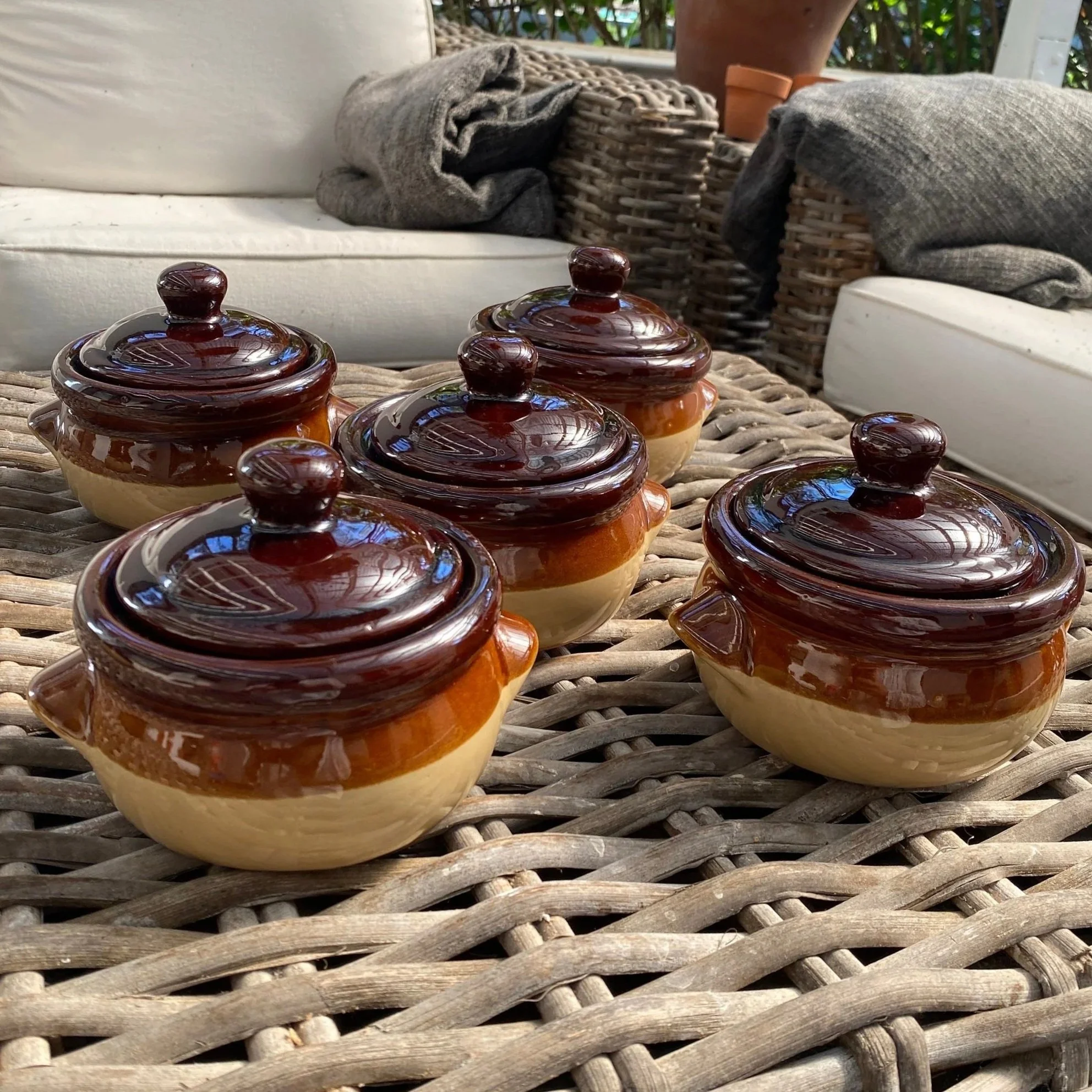 Five individual ramekins with lids arranged on wicker surface