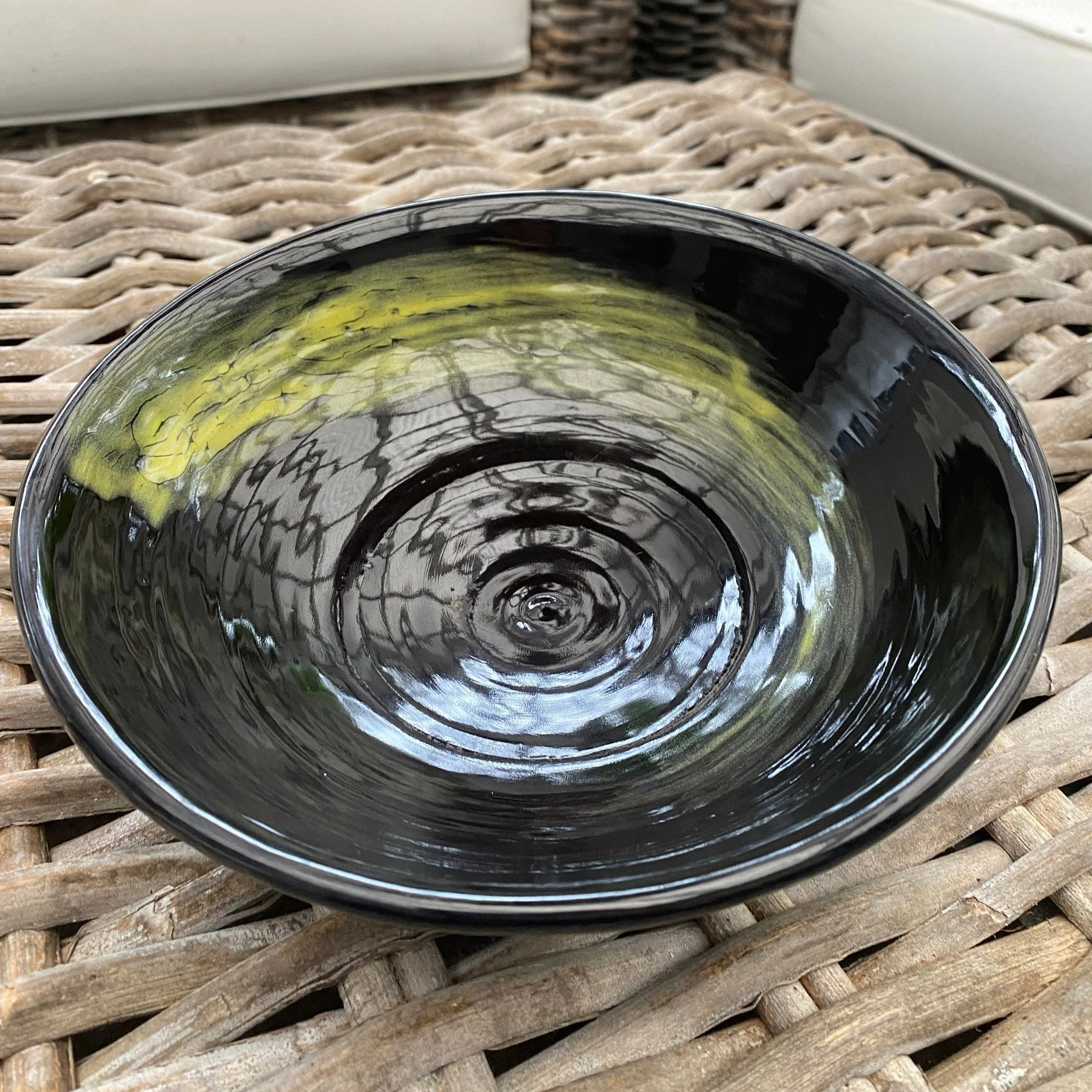Handcrafted ceramic dish in glossy black with yellow hand-painted swirl. Functional artisan piece perfect for serving or display – modern and unique.
