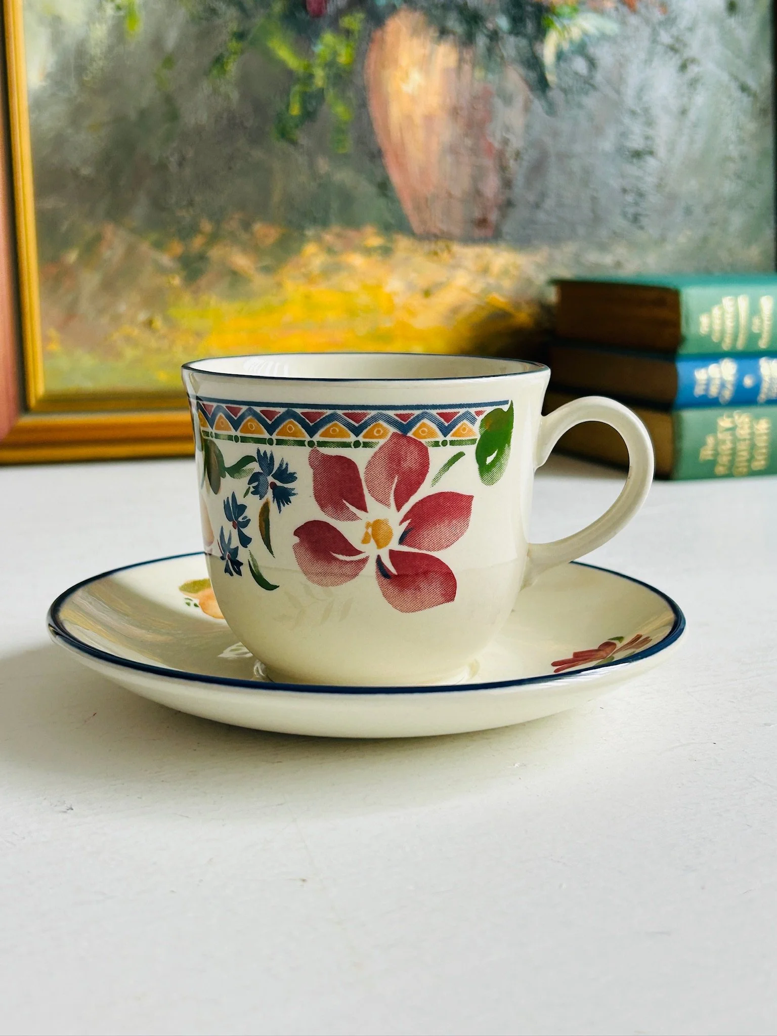 Staffordshire ‘Calypso’ vintage tea cup and matching saucer displayed together, showing the pink floral motif, geometric border, and blue rim.