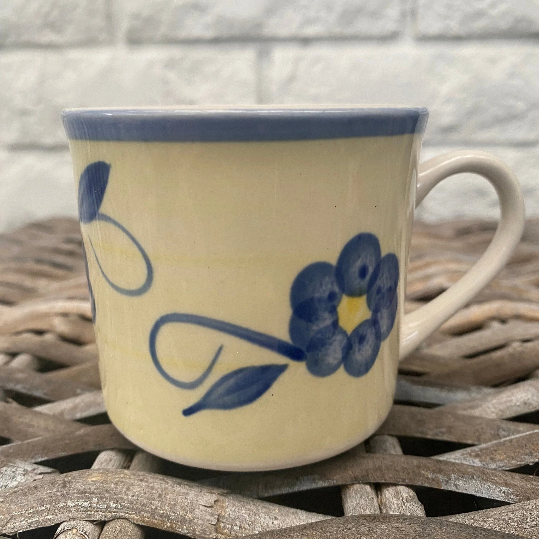 Front view of vintage yellow stoneware mug with blue flower motif and blue rim