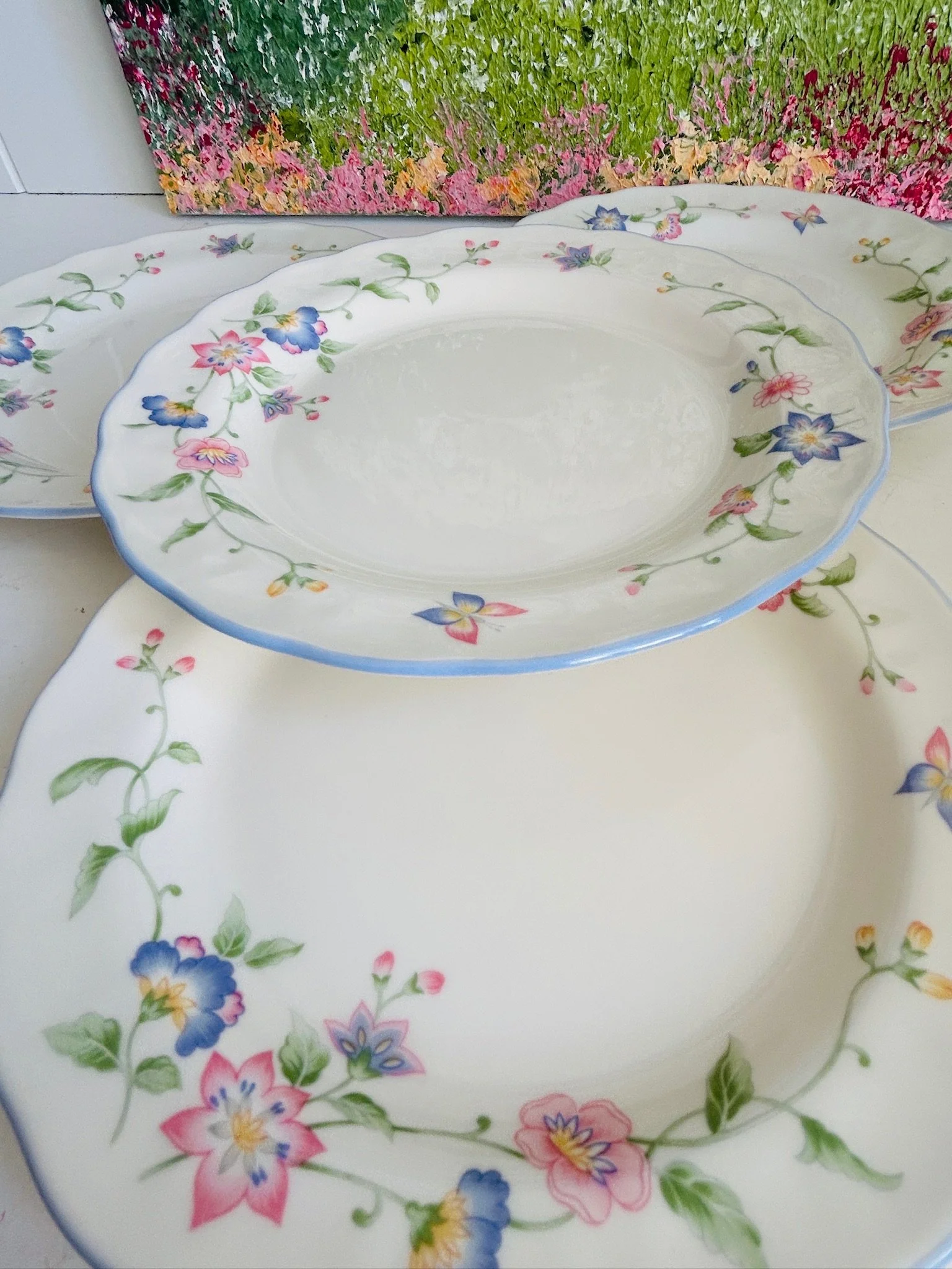 Angled view of one plate in front of matching pieces, highlighting the shallow form, floral decoration, and pale blue trim.