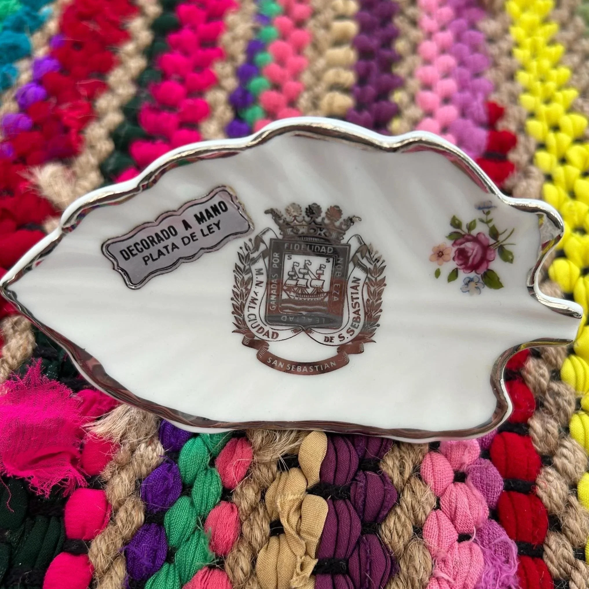 Decorative porcelain dish with San Sebastián crest and silver rim on colourful woven mat