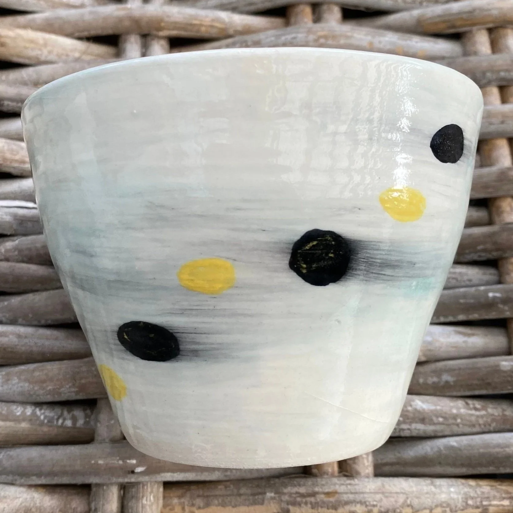 Side view of handmade pottery cup with yellow and black dots over soft glaze