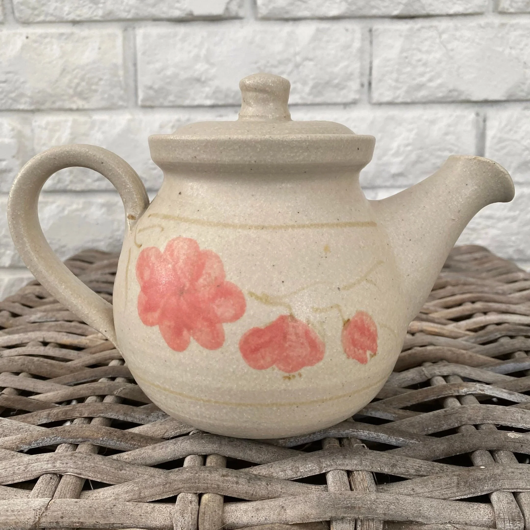 Side view of the beige teapot with hand-painted pink floral design, shown on a wicker background