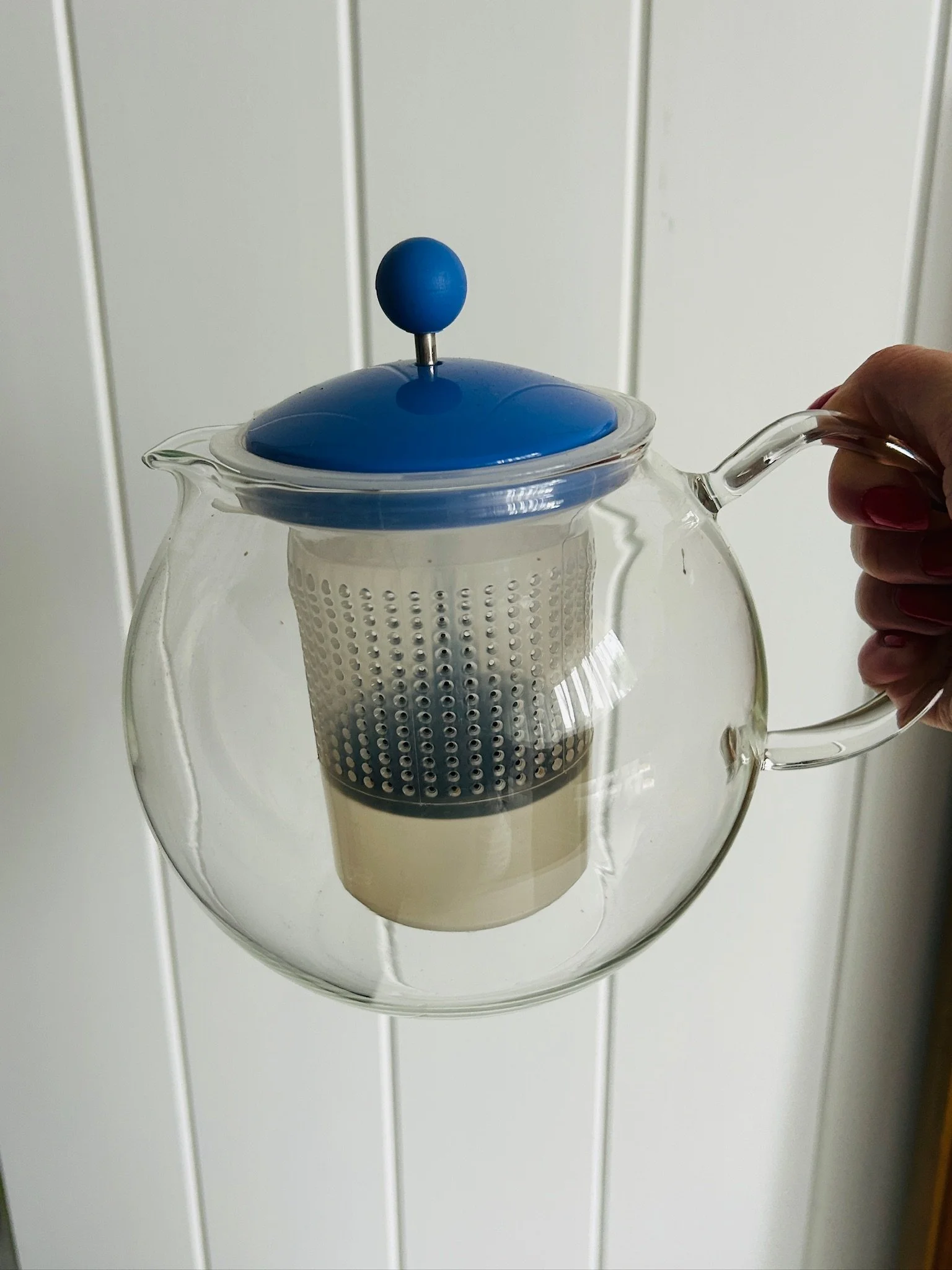 Close-up of the clear glass handle attached to the rounded teapot body.