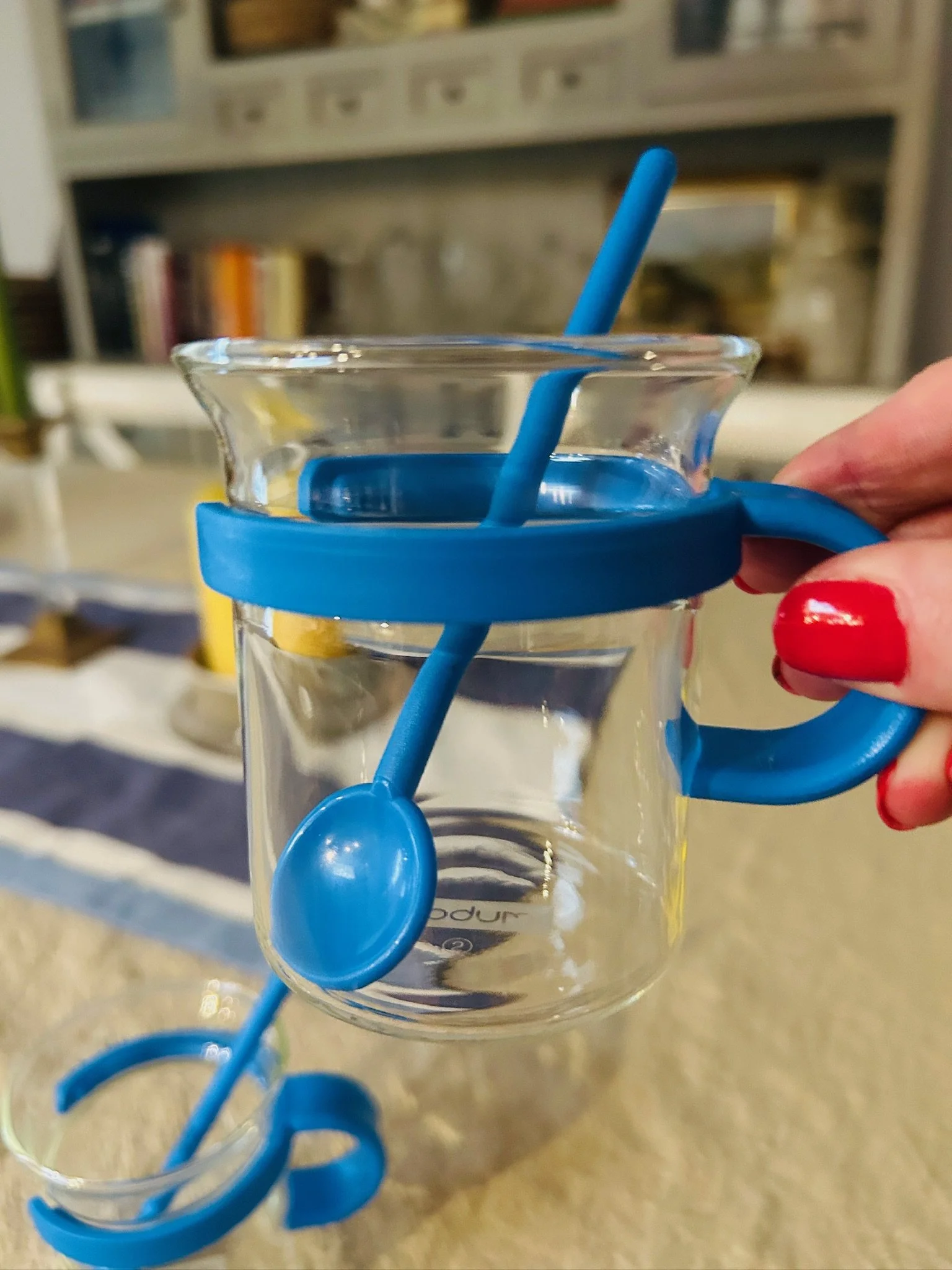 Close-up of a single blue Bodum Picard cup held by the handle, with the matching spoon placed inside the glass.