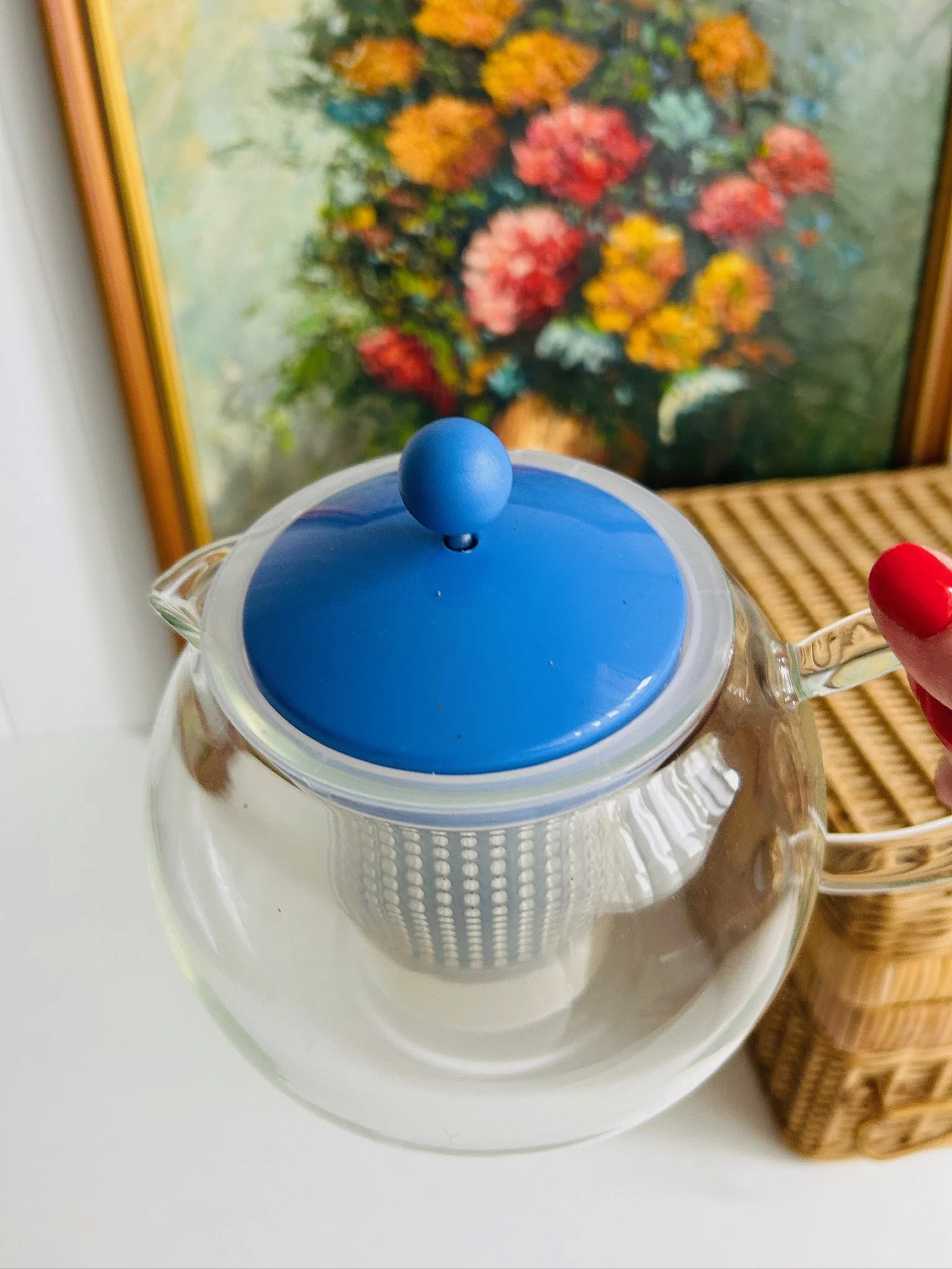 Angled side view of the Bodum Assam tea press held by the clear handle, with blue lid and infuser visible through the glass.