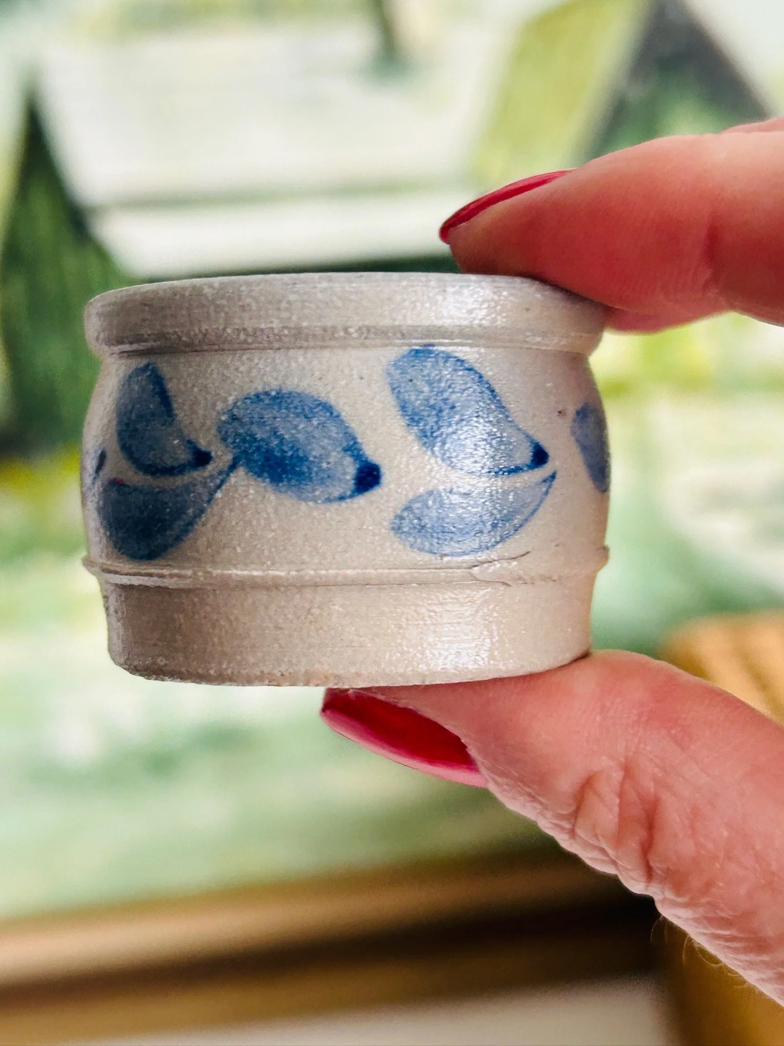 Side view of the salt cellar held between fingers, showing the blue leaf pattern wrapping around the taupe-grey stoneware body