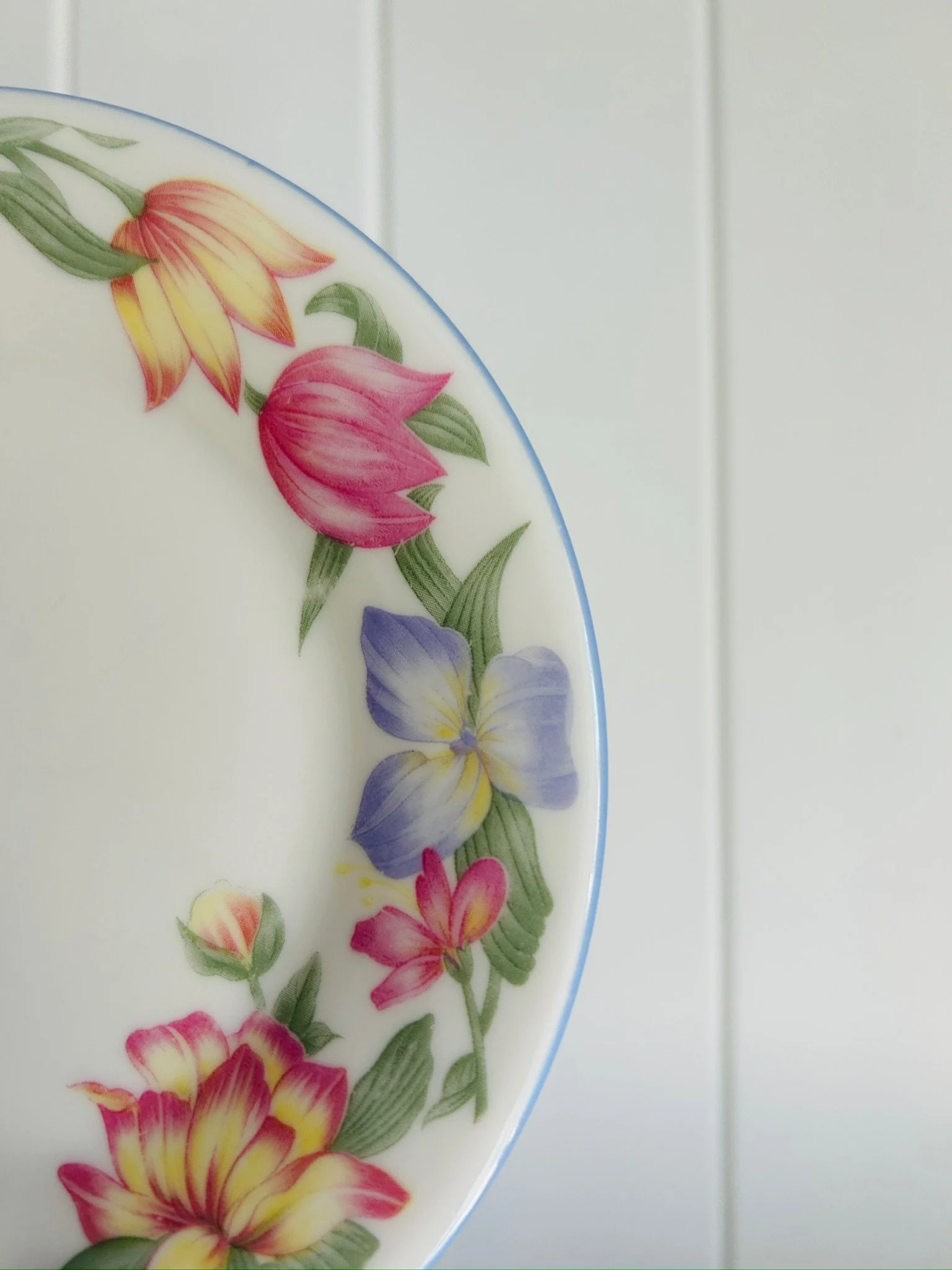 Close-up detail of the floral border, showing pink and yellow blooms, purple flowers, green leaves, and the fine blue rim