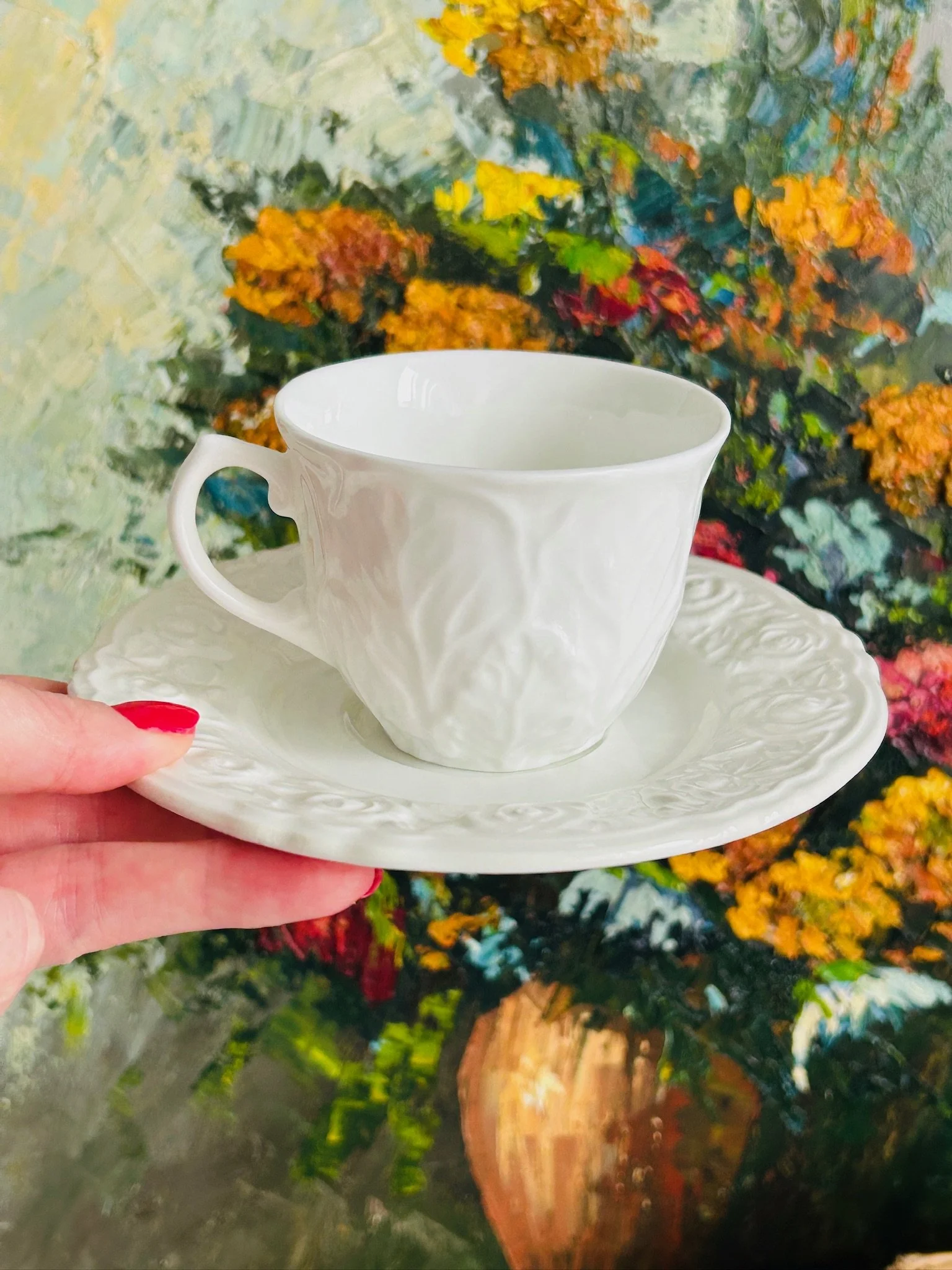 Front angle of the cup and saucer held in hand, showing the Wedgwood cup’s cabbage-leaf style embossing and the ornate saucer rim.