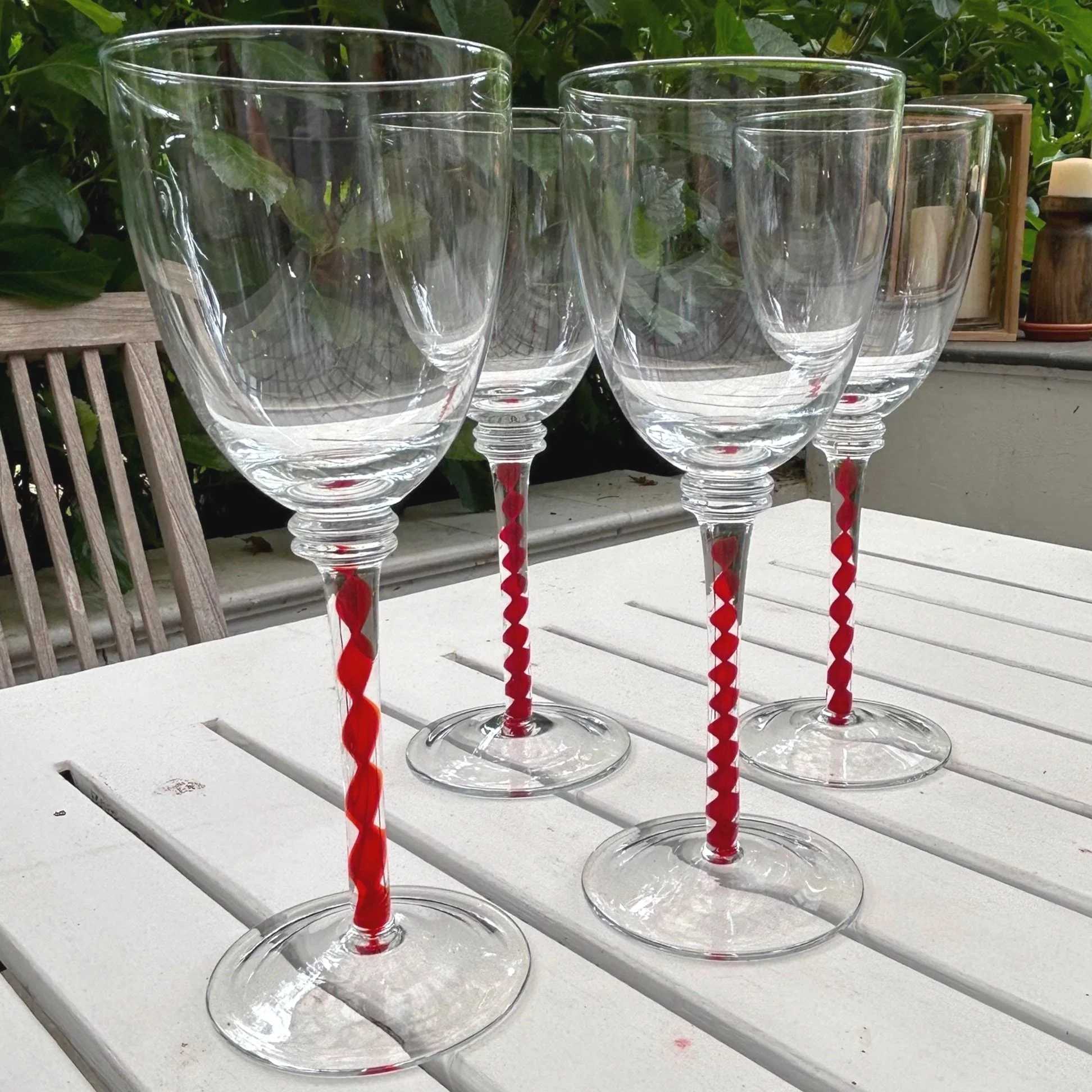 Full set of four wine glasses on white outdoor table with red twisted stems