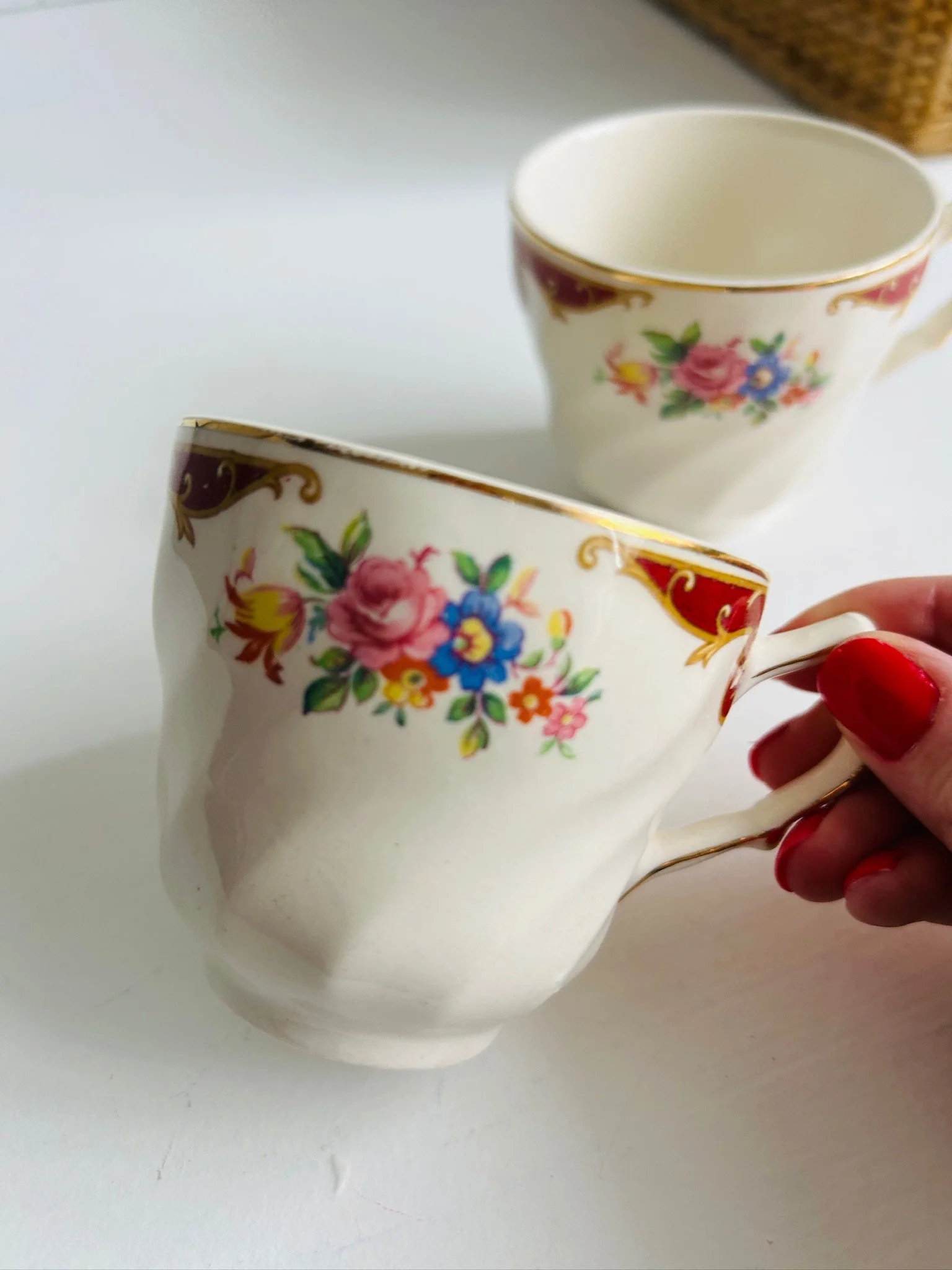 Another angled view of a teacup held in hand, highlighting the floral decoration, gold trim and elegant handle