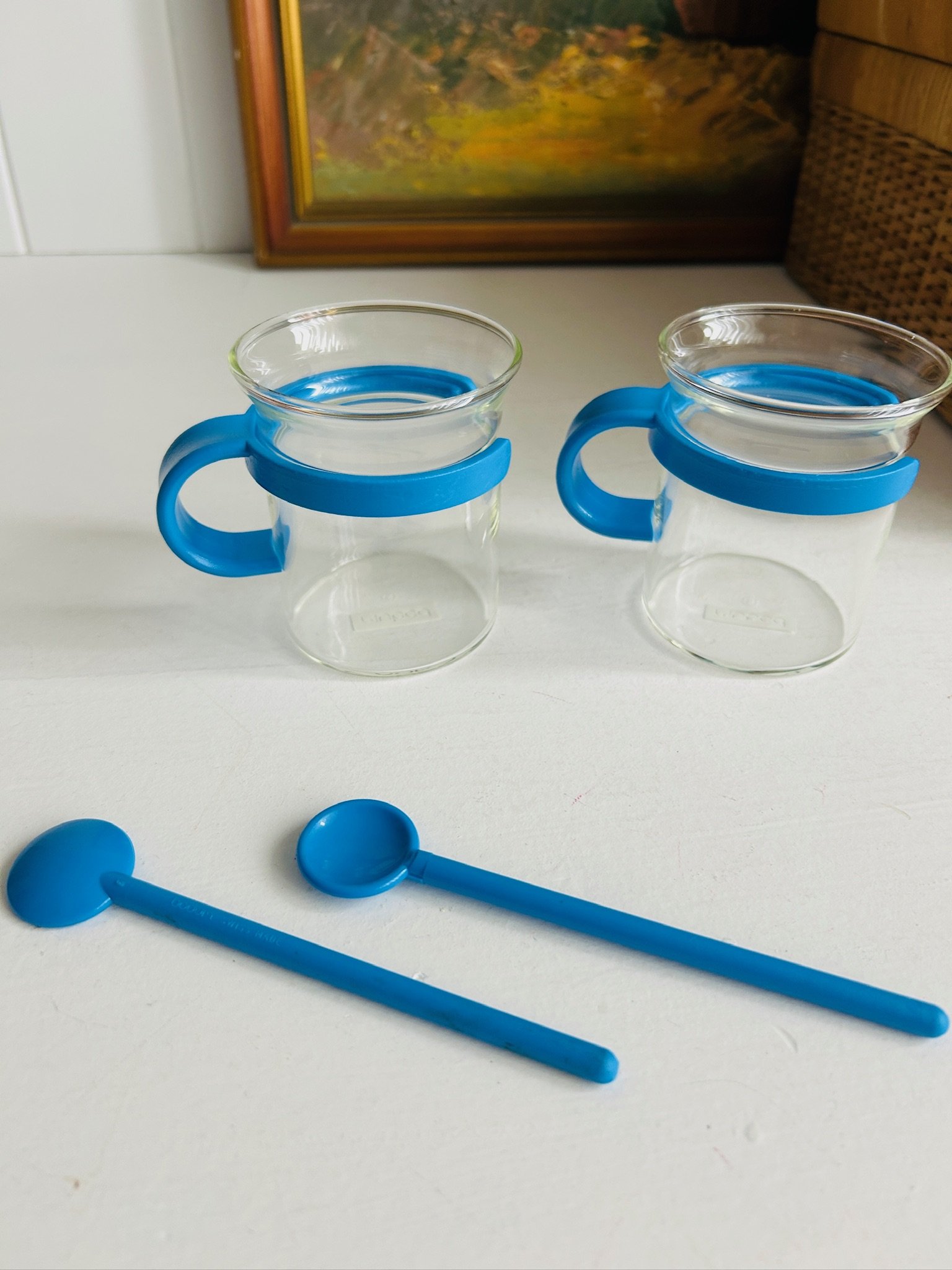 Angled view of two vintage Bodum Picard cups with blue holders, highlighting the curved handles and clear borosilicate glass.