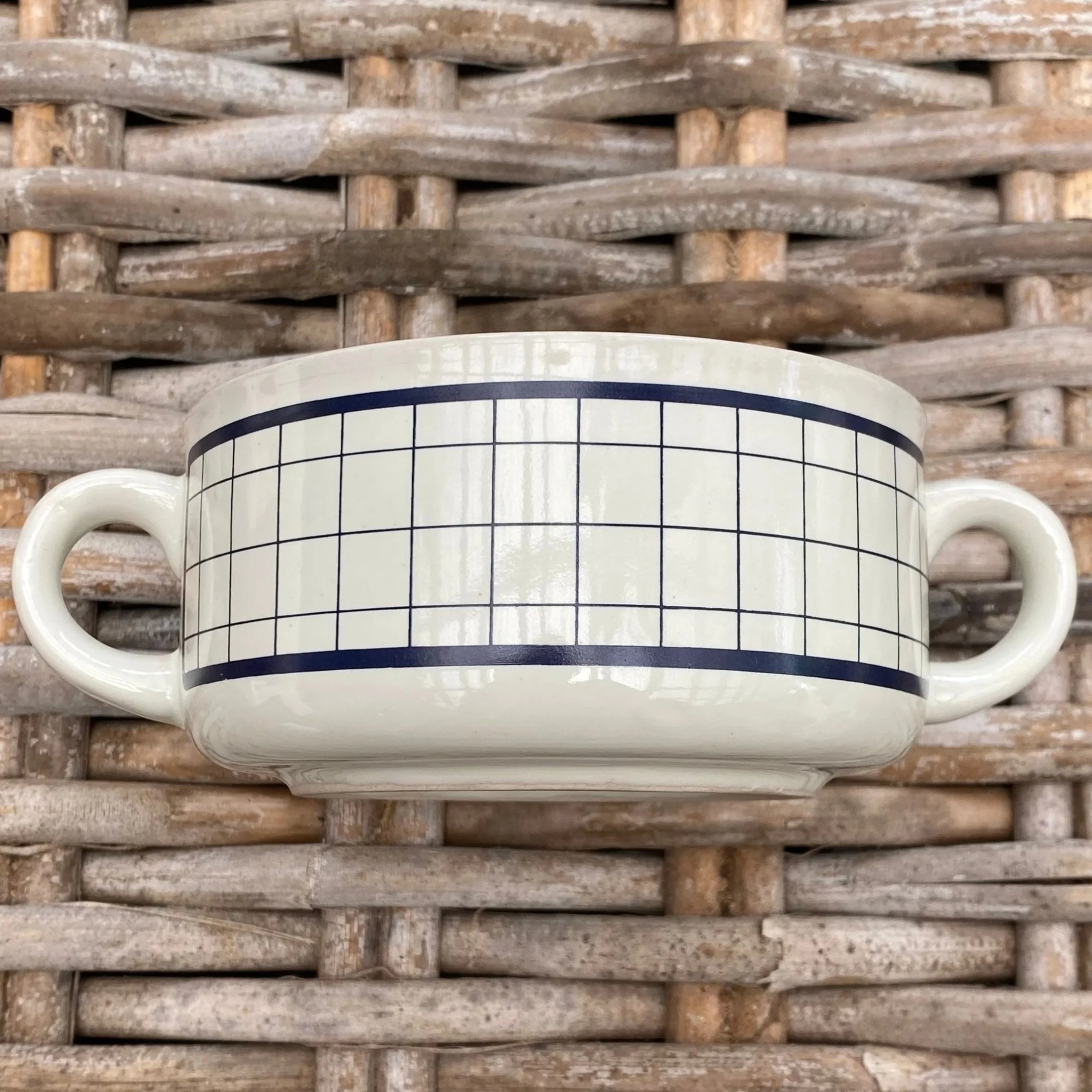 Blue grid pattern soup mug with twin handles on woven surface
