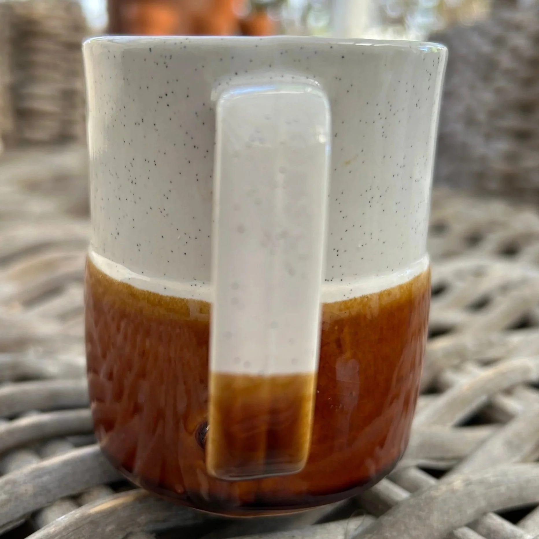 Side angle of the creamer being held, showing the profile, handle and glossy brown glaze