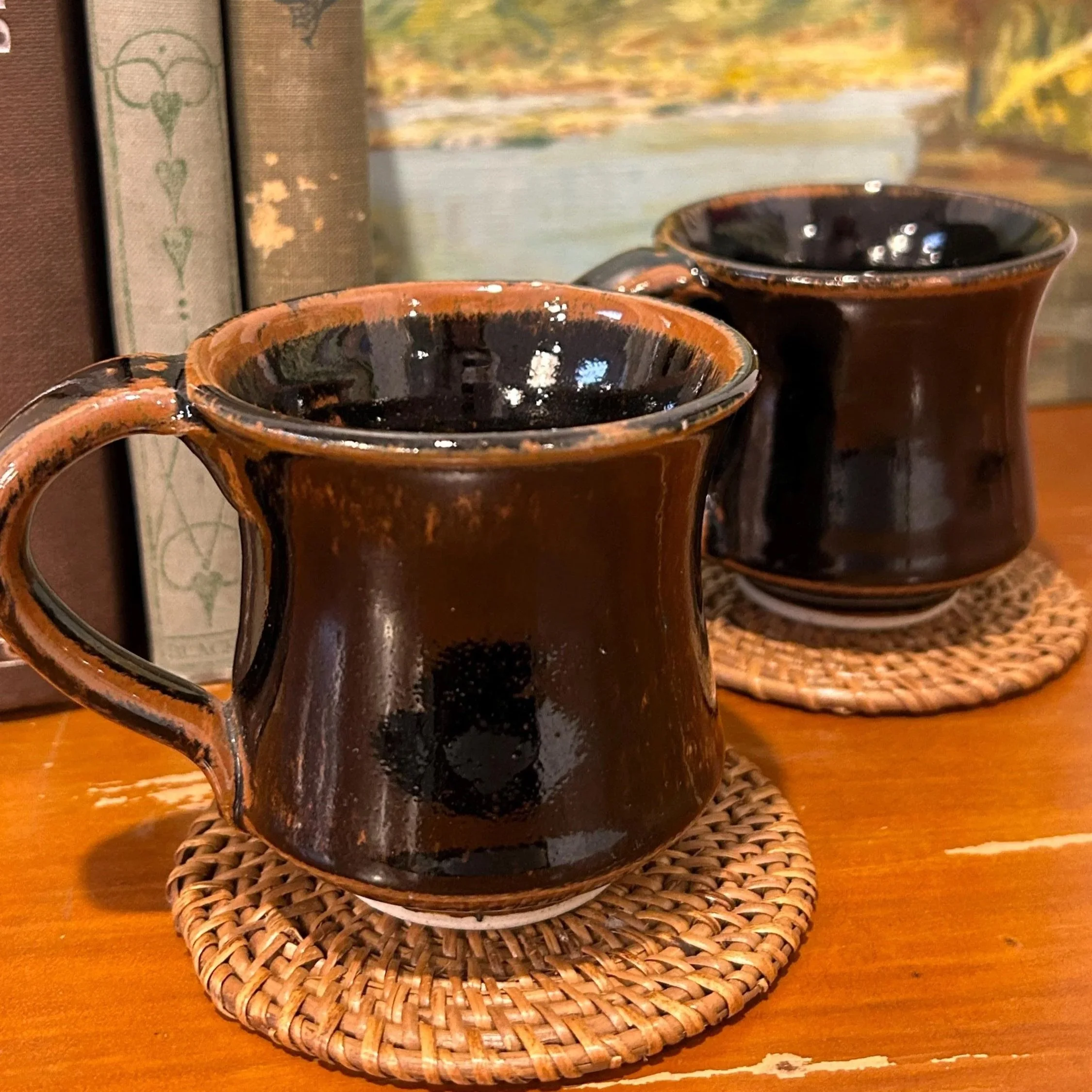 Pair of black glazed handmade mugs on woven coasters, side by side