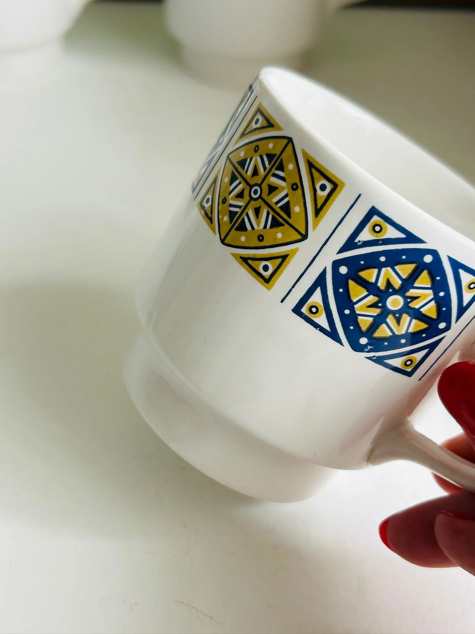 Close side view of a Staffordshire Midas cup showing the blue and mustard geometric design and white ceramic body.