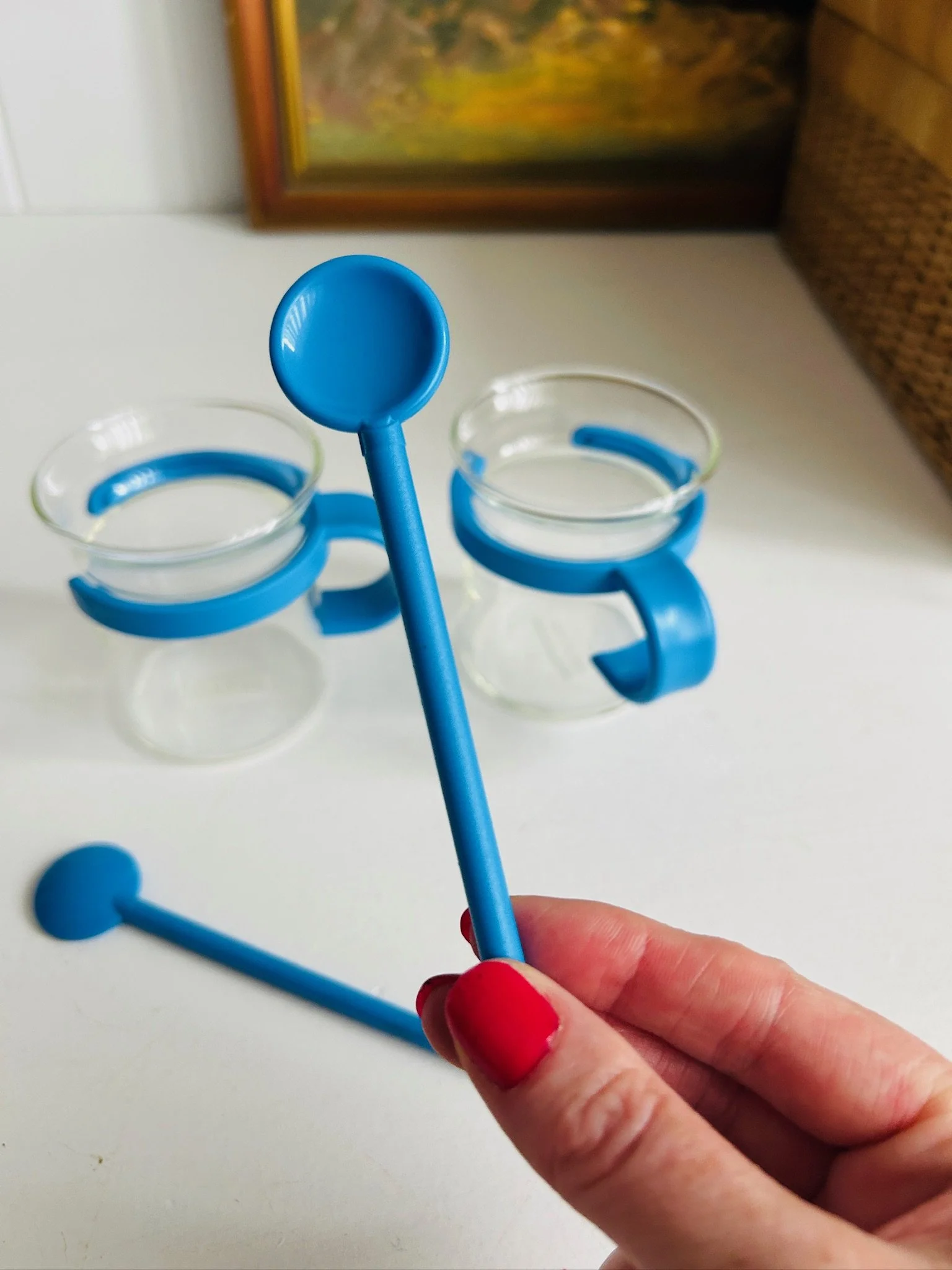 Close-up of a blue Bodum spoon held in hand, with two blue-holder Picard cups in the background.