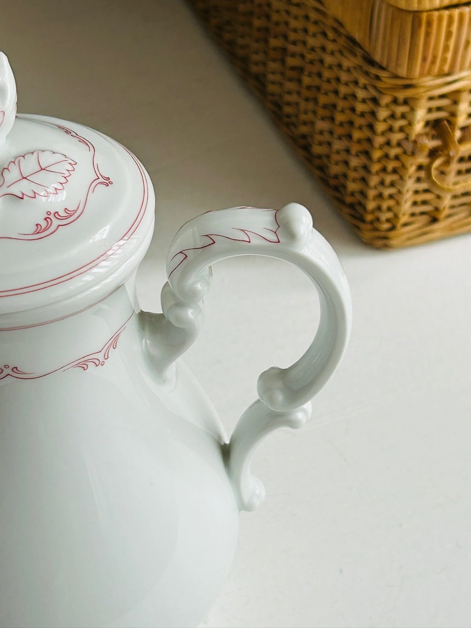 Side view focusing on the ornate handle and upper body, showing the red floral border and elegant porcelain form.