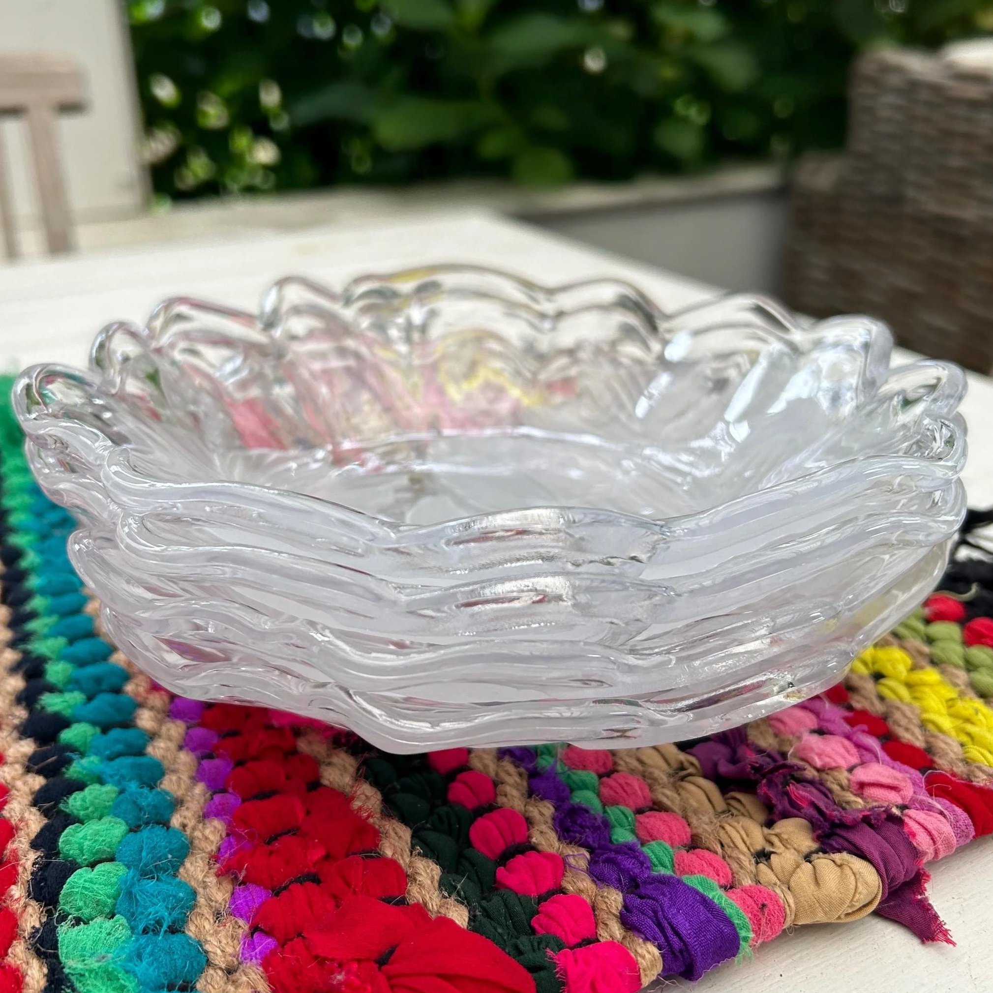 Set of clear scalloped crystal bowls resting on a colourful woven mat.