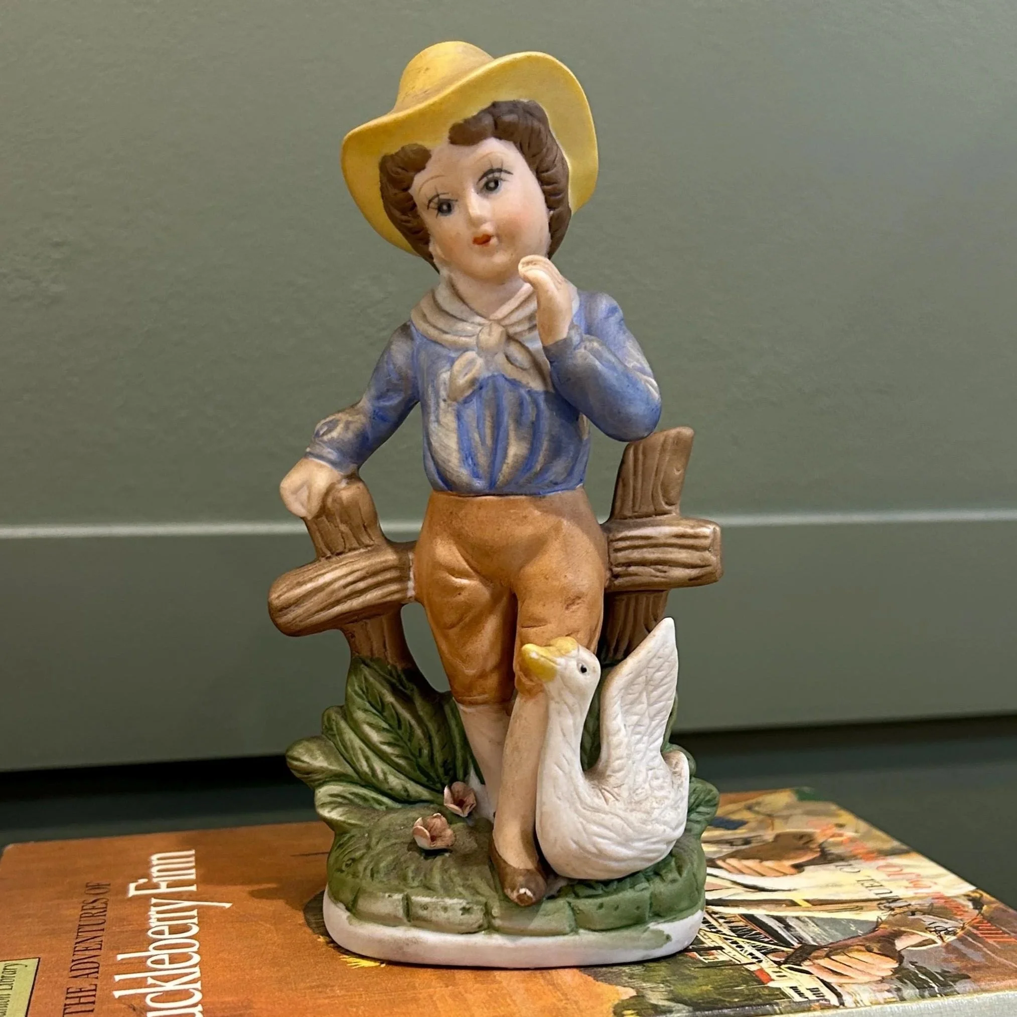 Front view of porcelain figurine with boy leaning on fence and white goose at his side