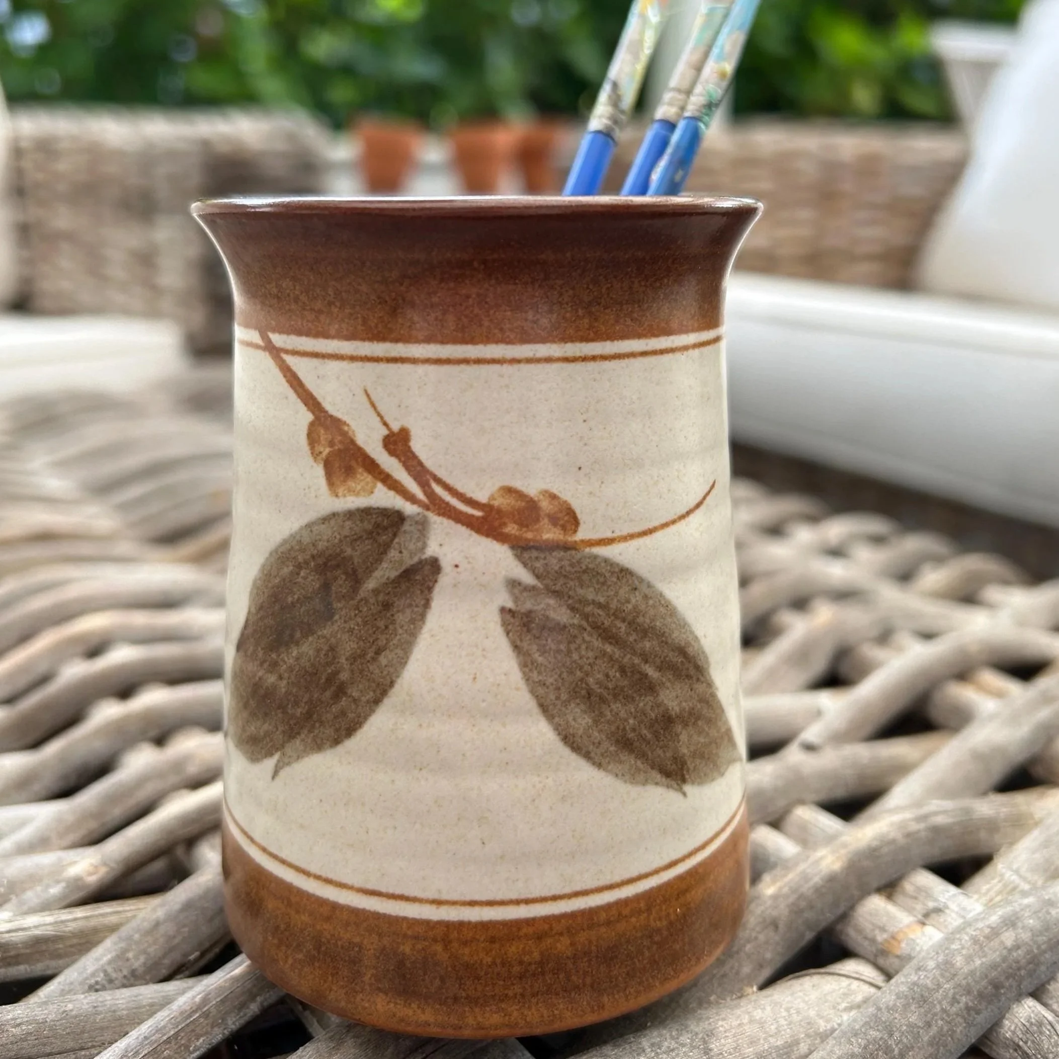 Handmade pottery jar with leaf design, shown holding spaintbrushes outdoors