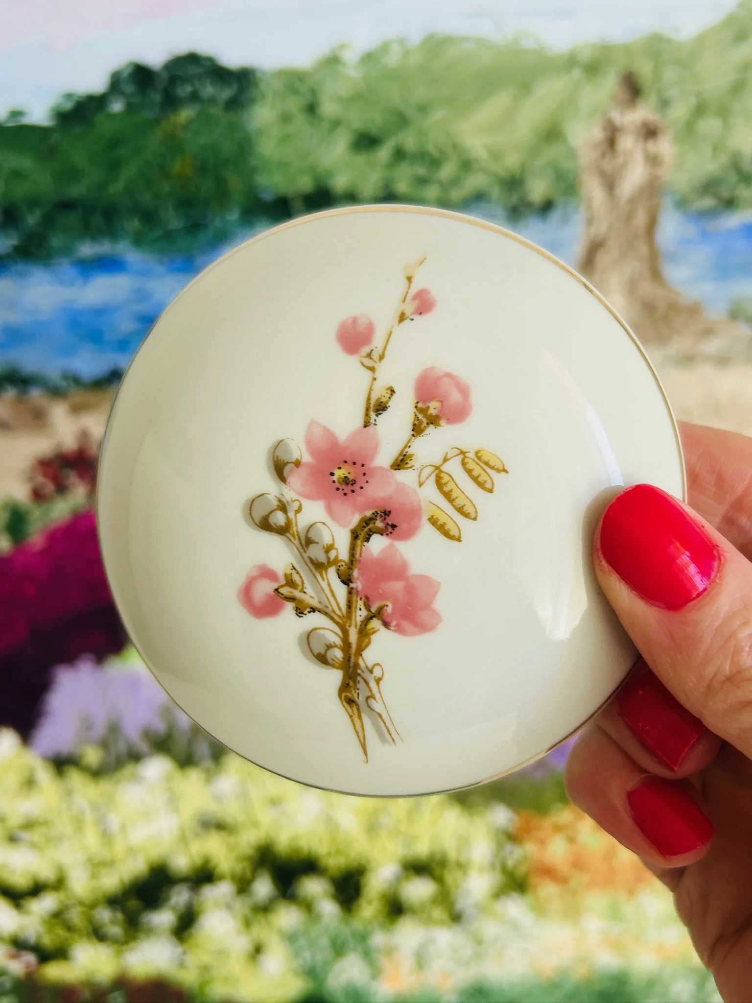 Top view of the lid held in hand, highlighting the pink blossom motif, brown stems, and gold botanical detailing