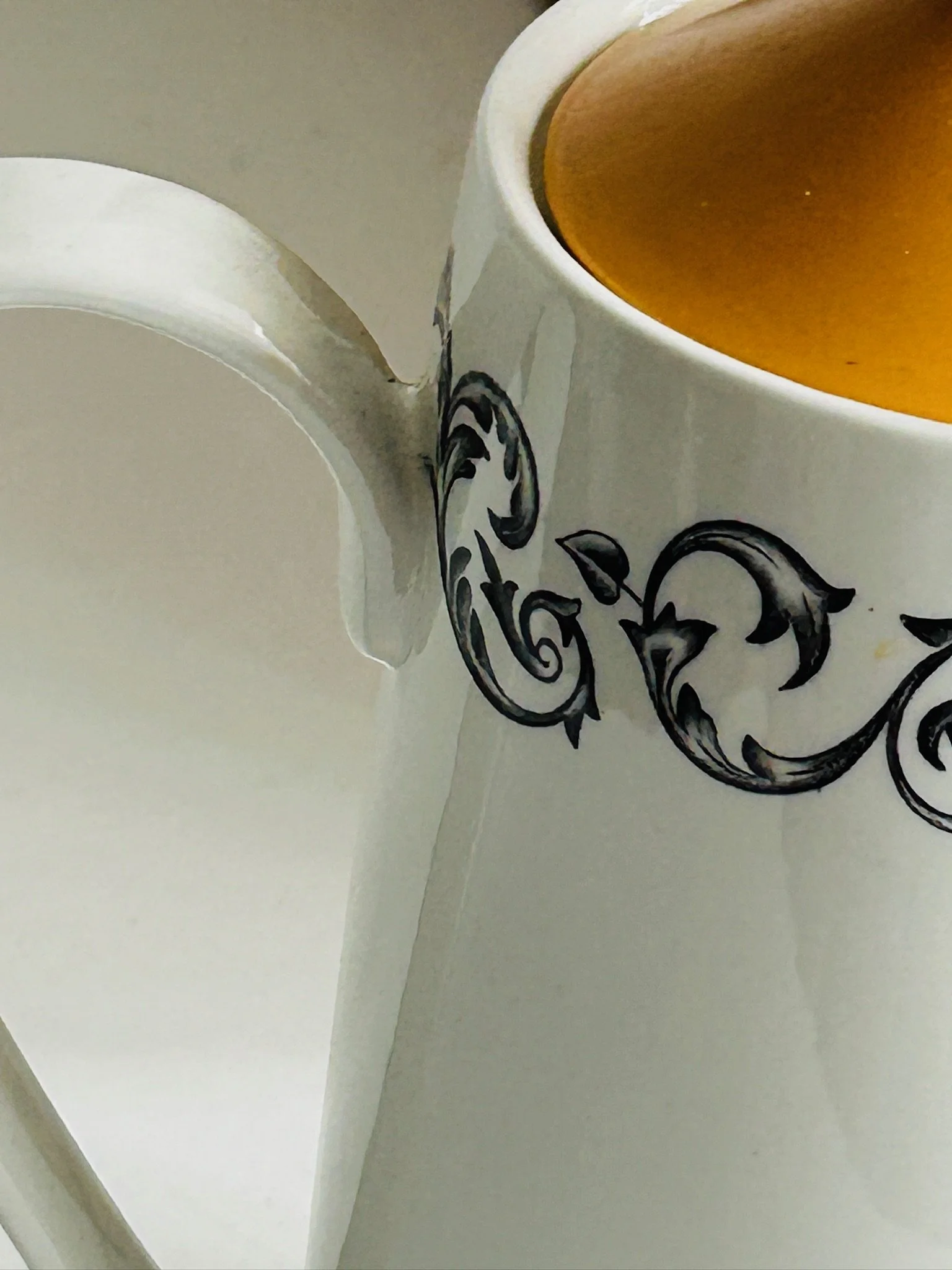 Detail shot of the spout and rim pattern, showing the glossy white finish, black scroll design, and orange interior glaze.