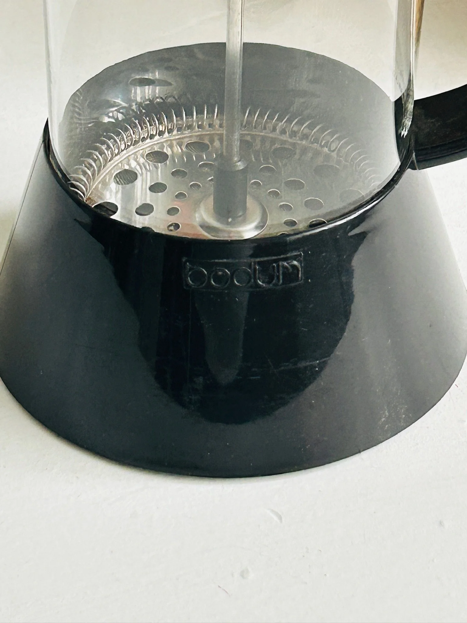 Close-up of the lower black plastic frame showing the embossed Bodum logo and the metal filter plate inside the carafe.