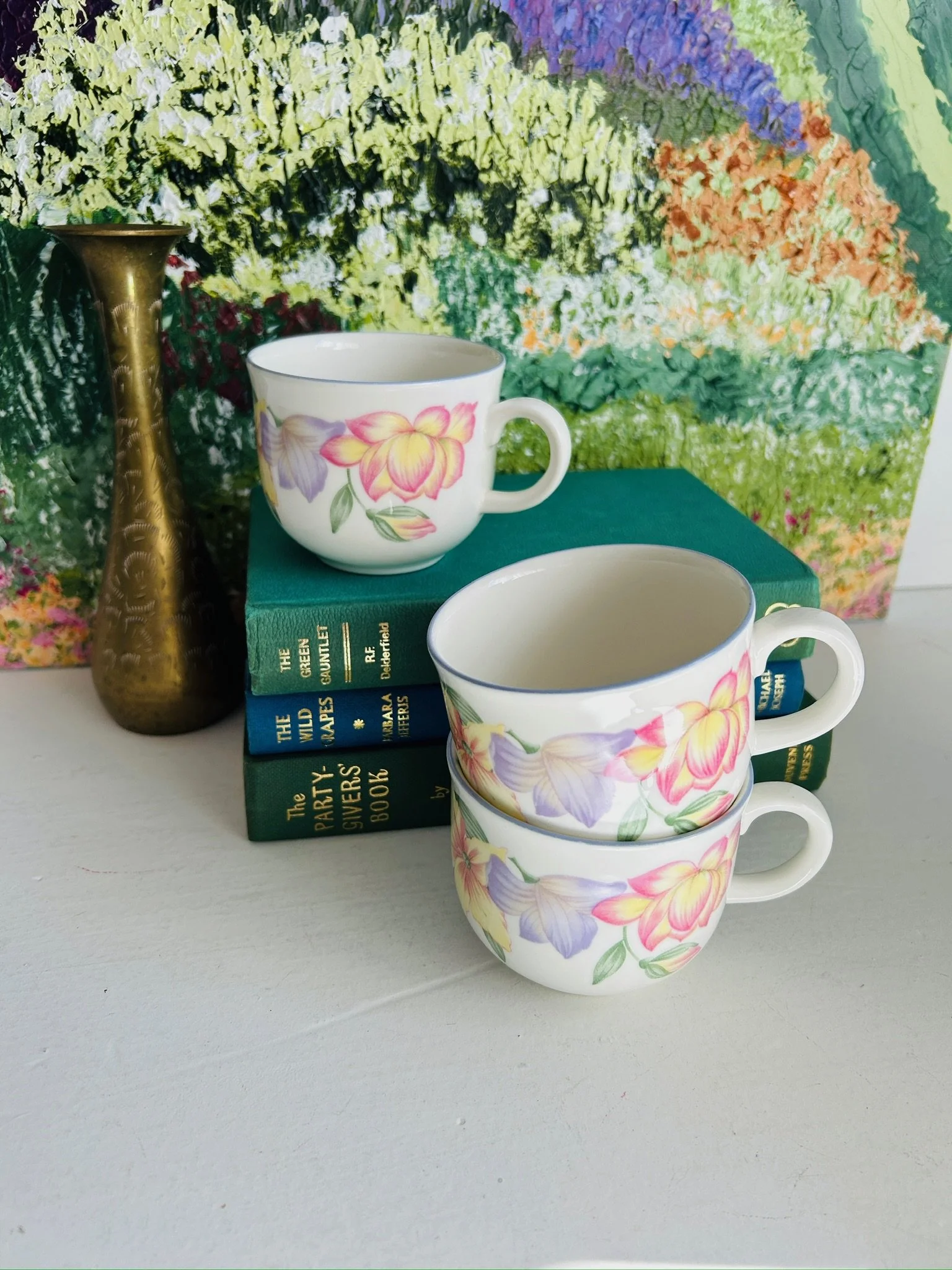 Grouped display of three vintage floral teacups styled on books, showing the set together from a different angle