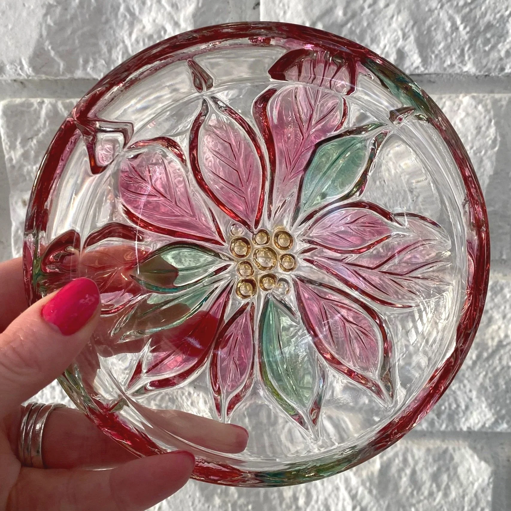 Clear glass dish with pink and green poinsettia design held in hand.