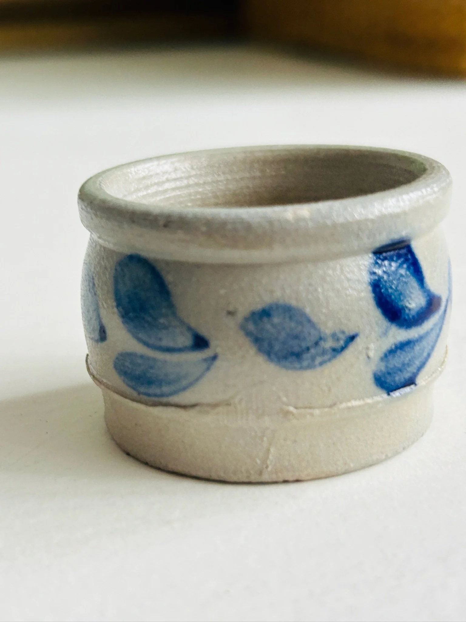 Close-up front view of the handmade stoneware salt cellar with blue leaf motif, showing the rolled rim and painterly decoration