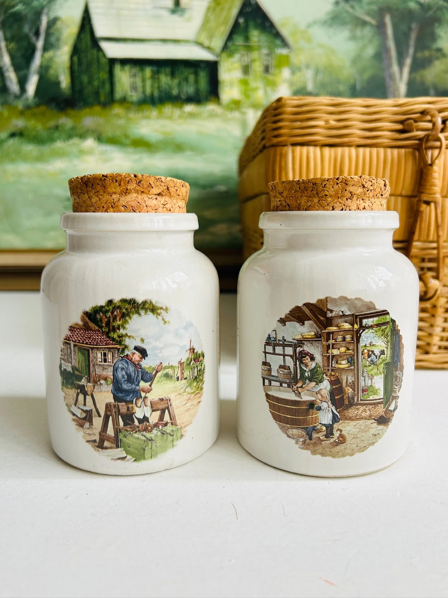 Two ceramic pots displayed side by side with cork lids in place, showing the matching artisan-made form and hand-painted scenes.