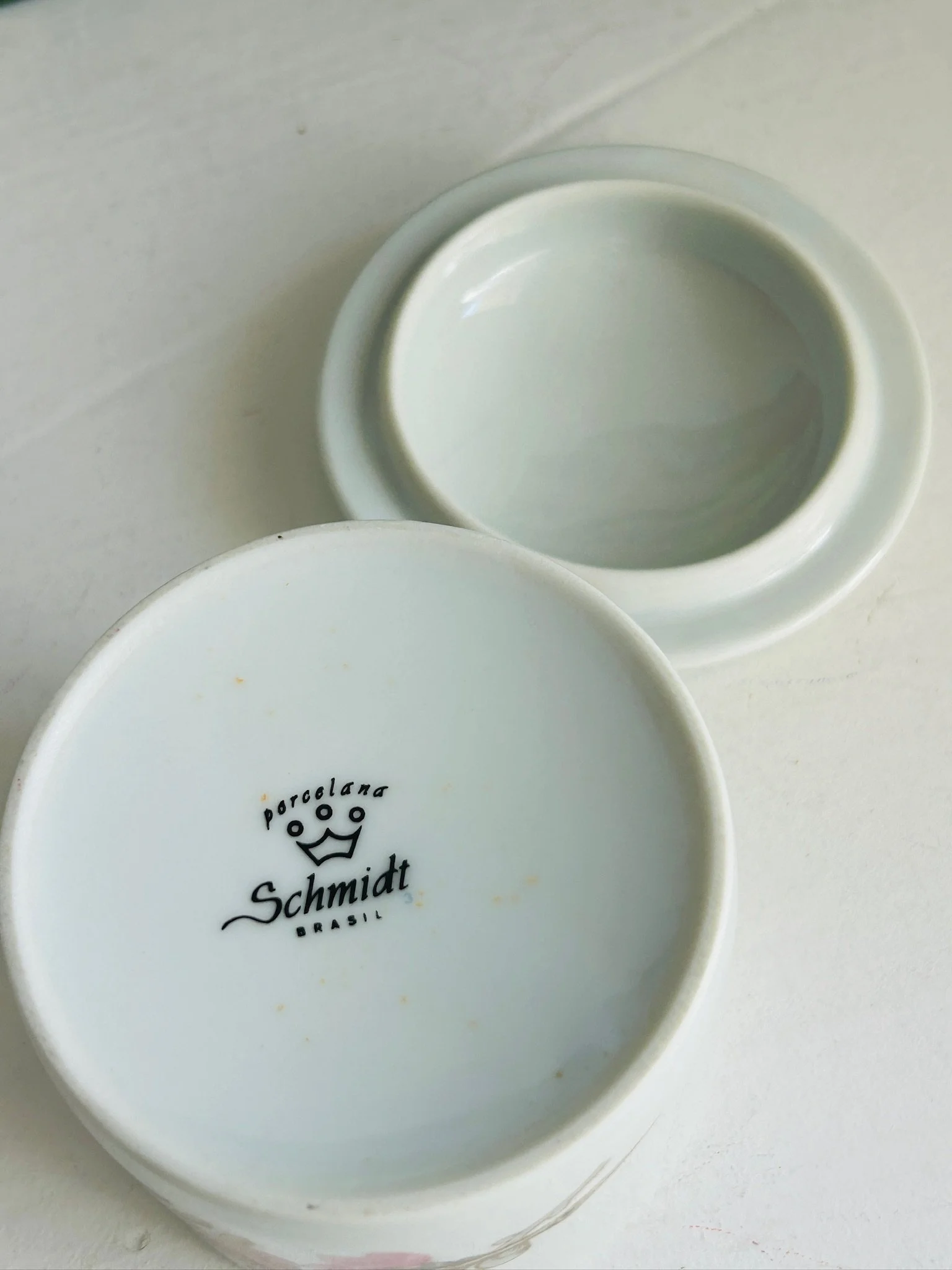 Underside view of the trinket bowl and lid, showing the Porcelana Schmidt Brazil backstamp on the base and the plain white glazed interior of the lid