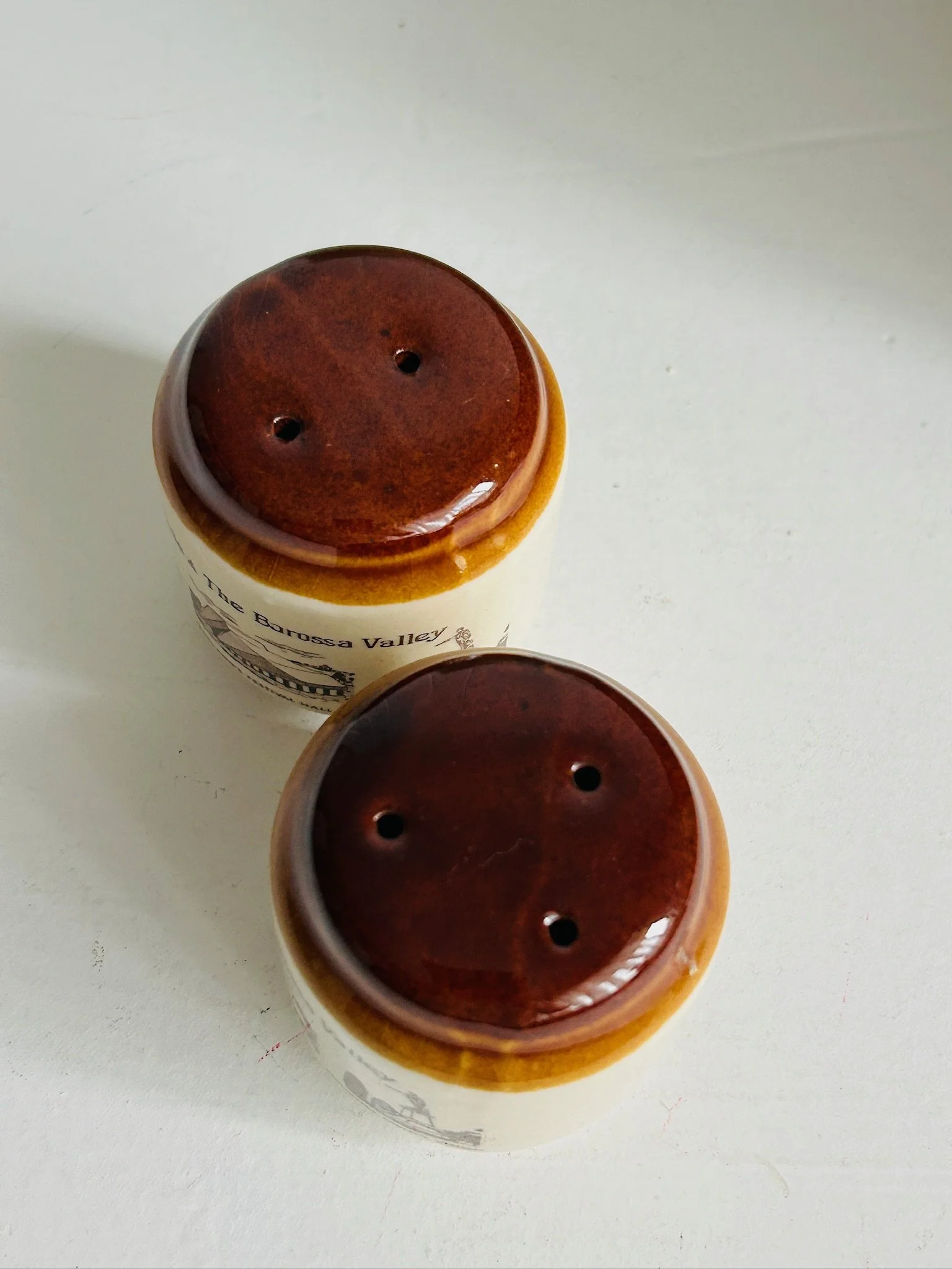 Top-down view of both shaker tops, showing the different hole patterns for salt and pepper in glossy brown glaze.